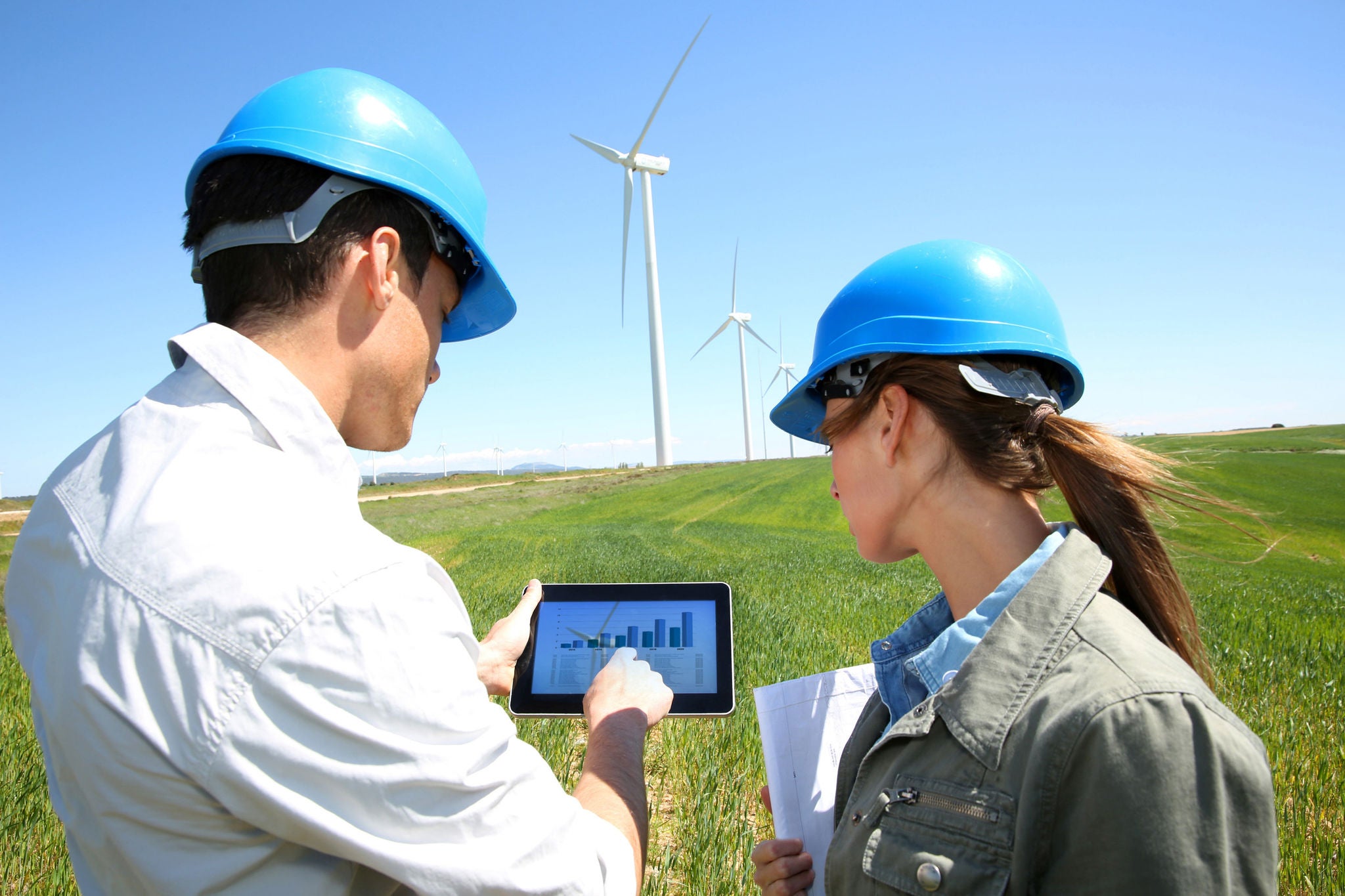 People looking at tablet wind turbines in background