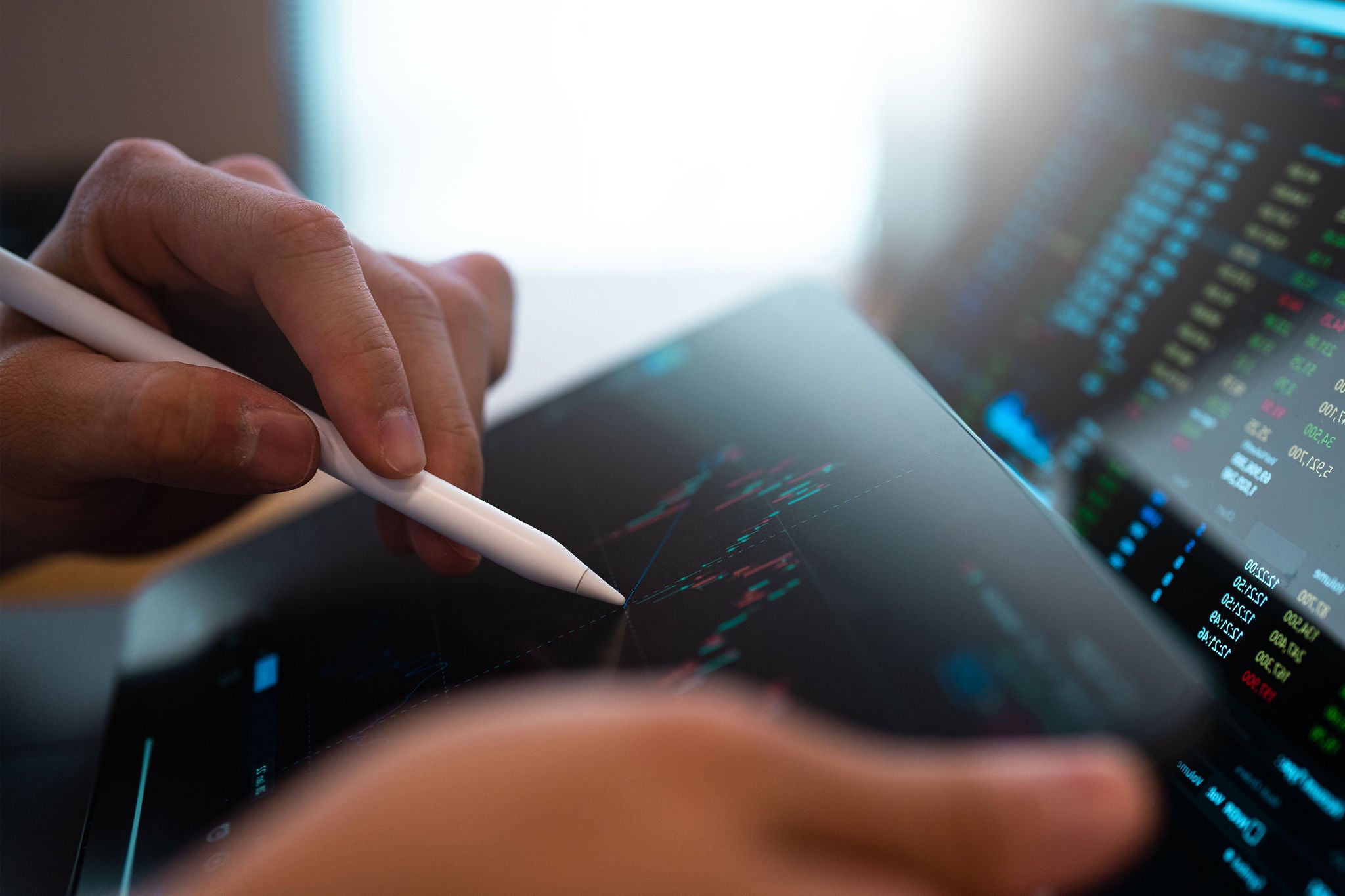 Person hält Tablet-Stift über Bildschirm mit Datenanalyse und Finanzdiagrammen.