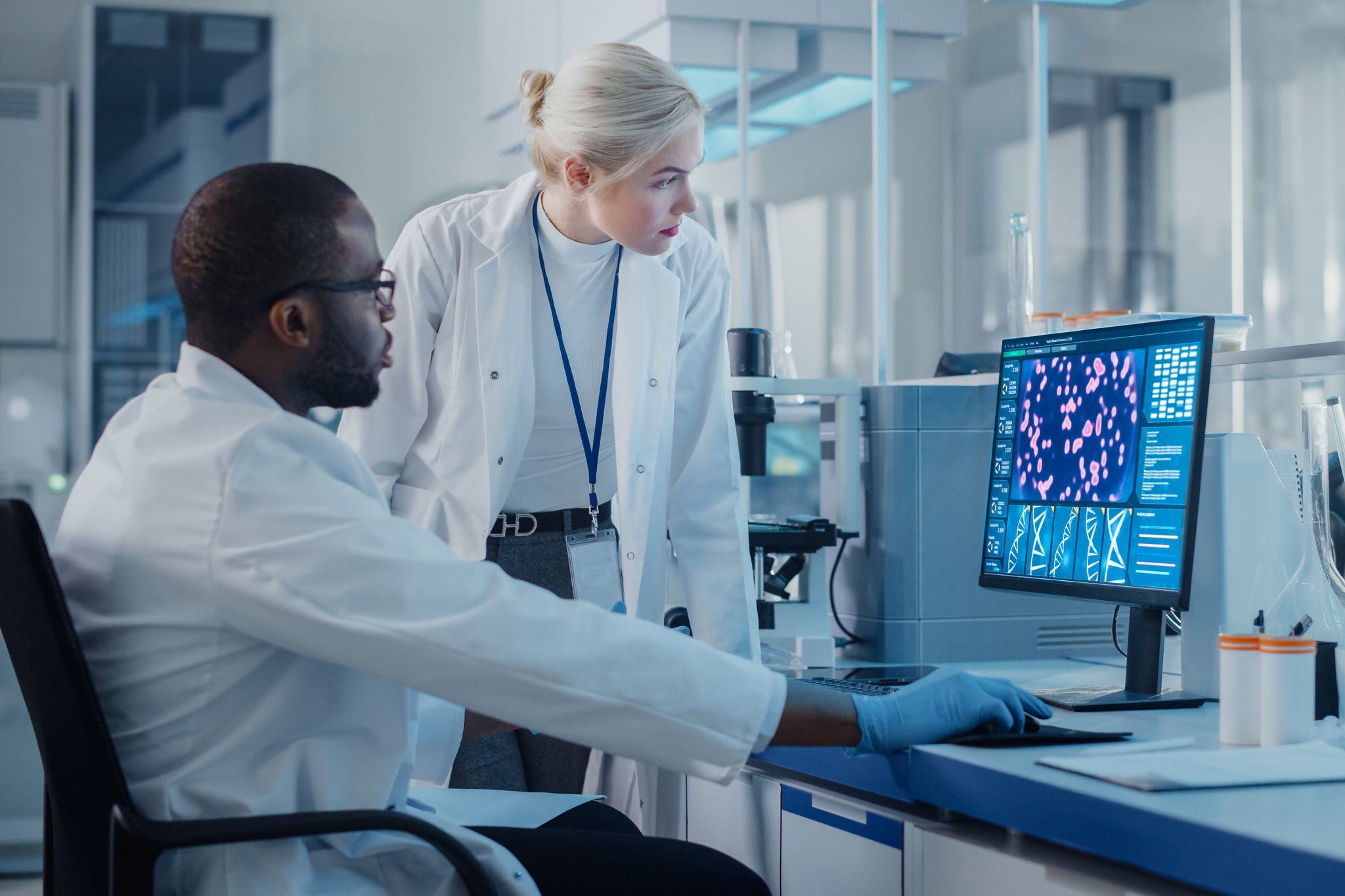 Modern Medical Research Laboratory: Two Scientists Use Computer with Screen Showing DNA Gene Analysis, Specialists Discuss Innovative Technology. Advanced Scientific Lab for Medicine, Biotechnology