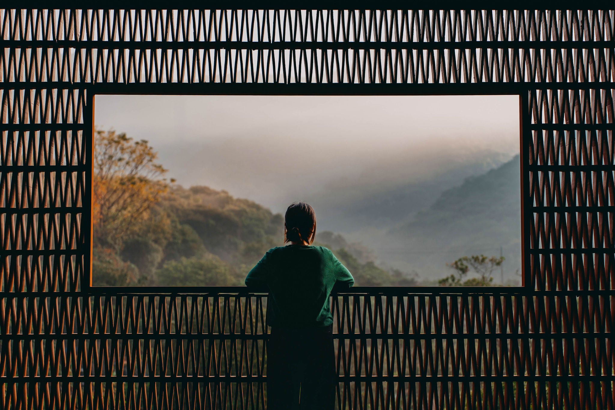 Rear view of young Asian woman enjoying the spectacular scenery during sunrise from a Chinese style balcony with traditional pattern and looking into the distance. Travel and vacation. Exploration and discovery concept