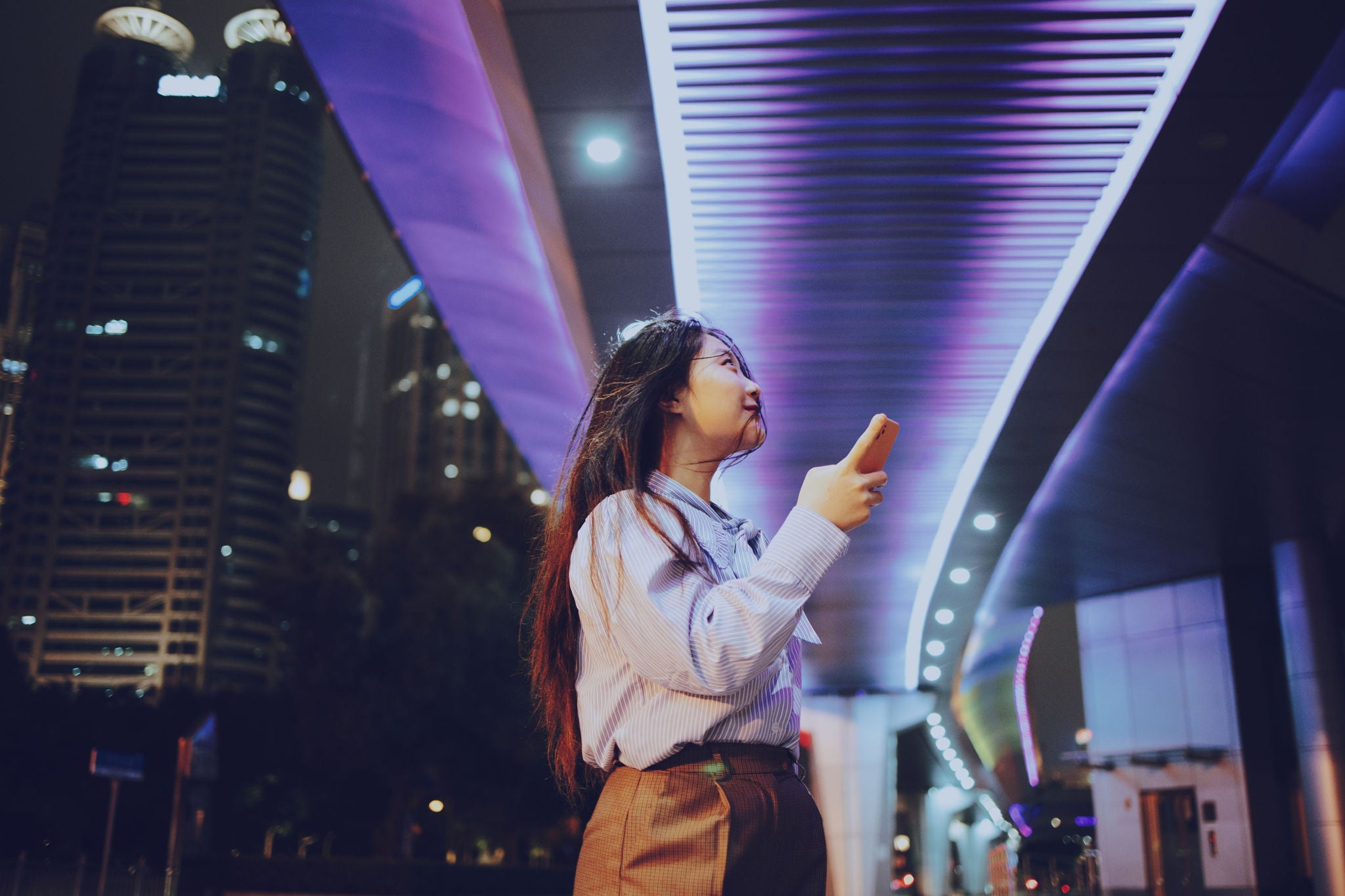 Person mit Smartphone unter moderner Architektur und LED-Beleuchtung bei Nacht.