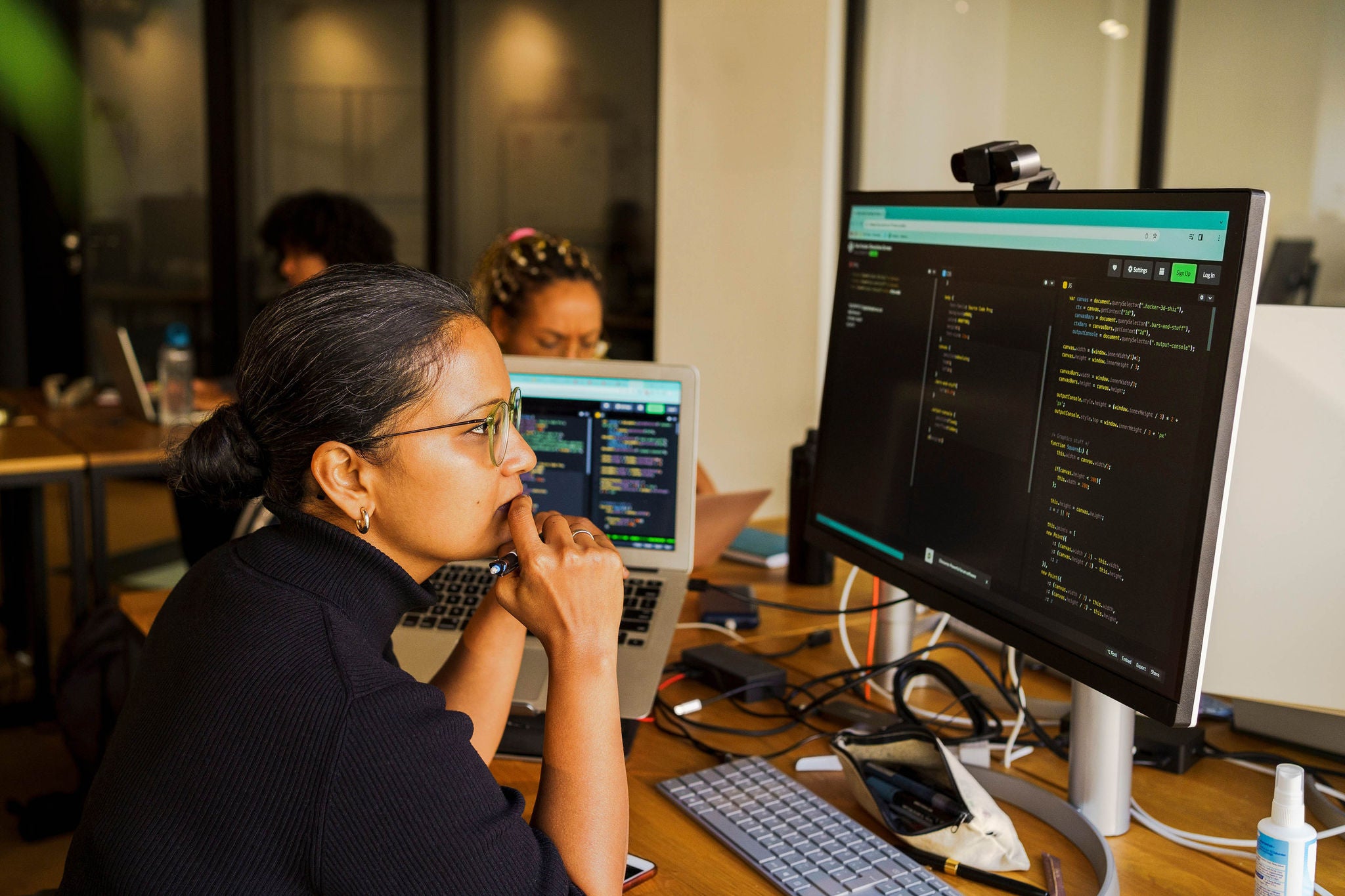 Thoughtful female coder looking at desktop PC while sitting in startup office