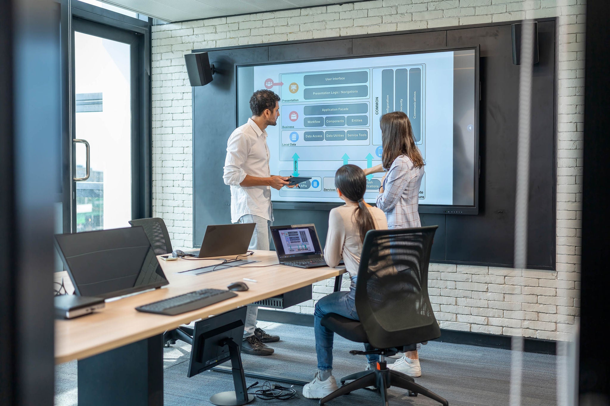 Male software developer presenting the Mobile Application Architecture Diagram on the large screen to developer team in meeting room.