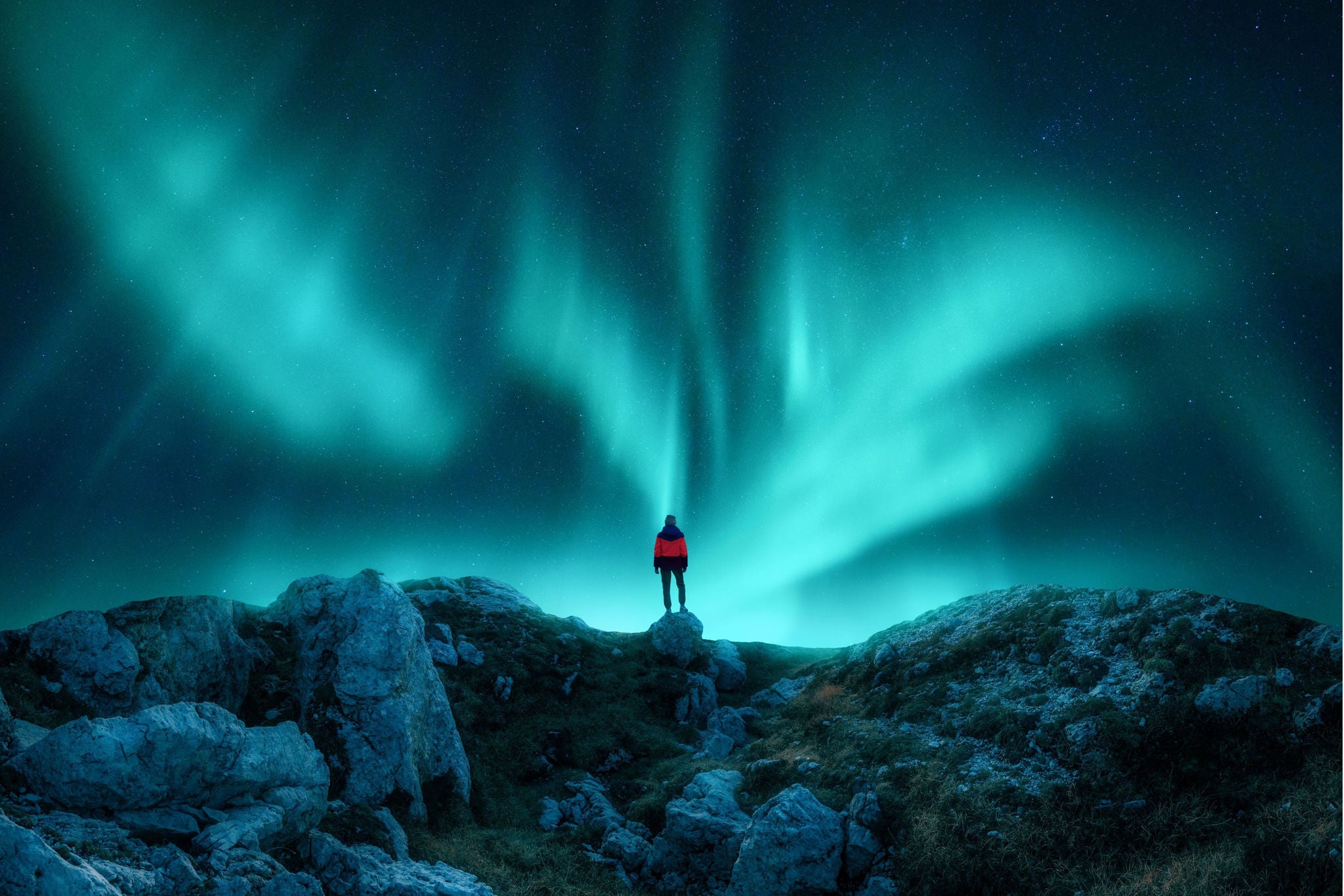 Person auf Felsen unter leuchtenden Nordlichtern am klaren Nachthimmel.