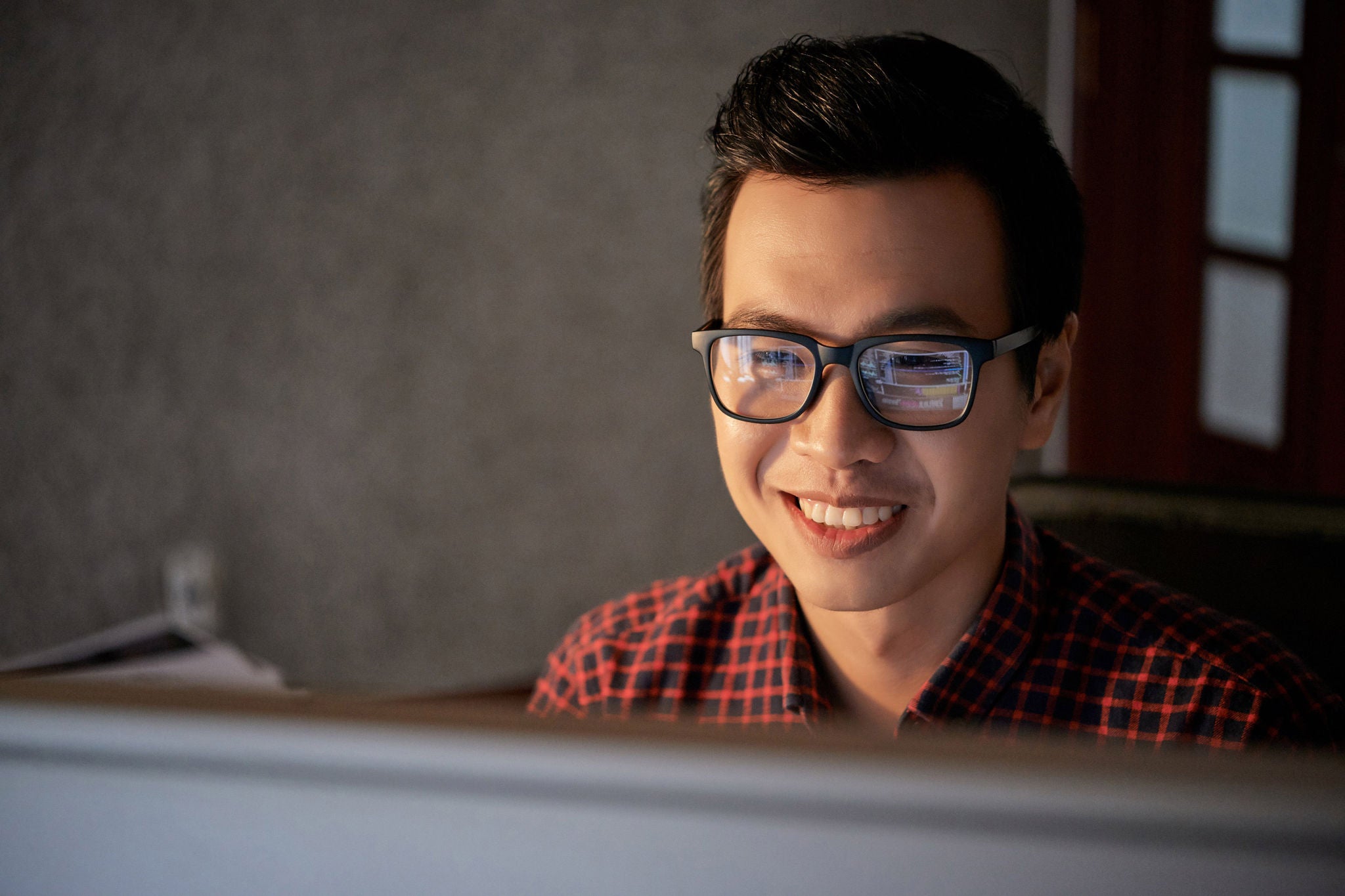 Happy young Asian software developer reading e-mails from grateful clients
