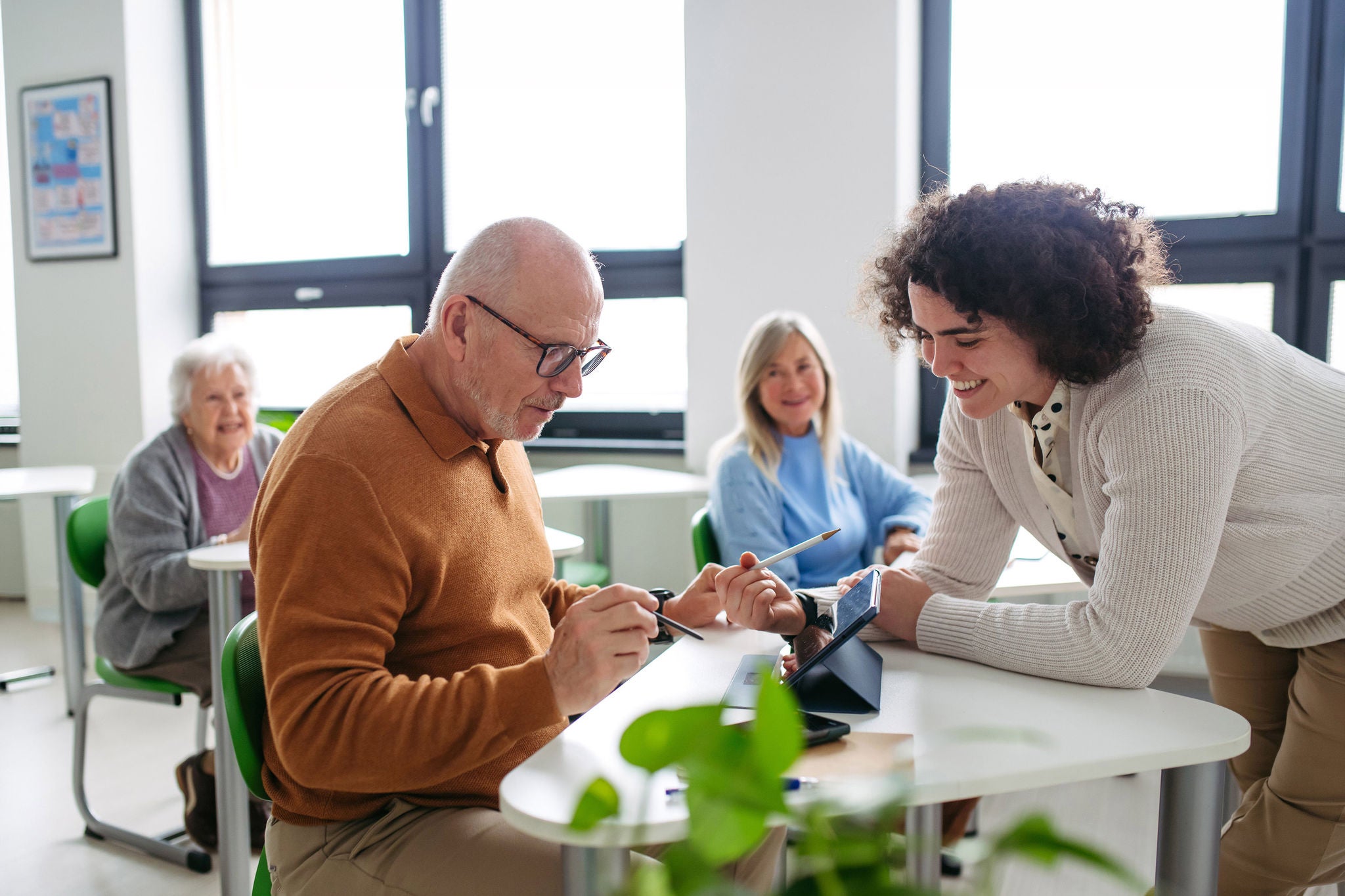 Female tutor helping senior man to learn digital skills in community center.