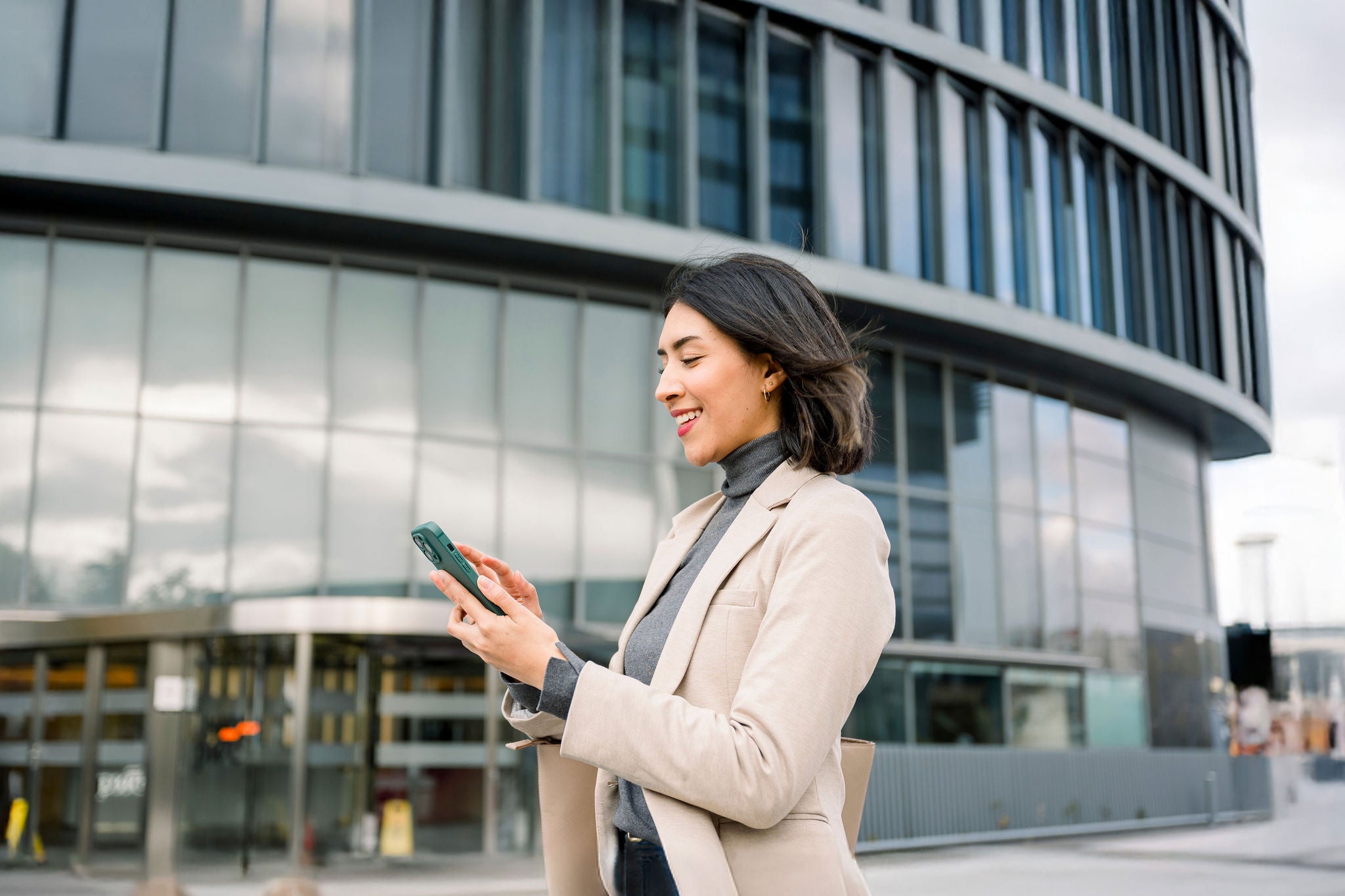 Businesswoman using mobile phone outdoors in front of modern building