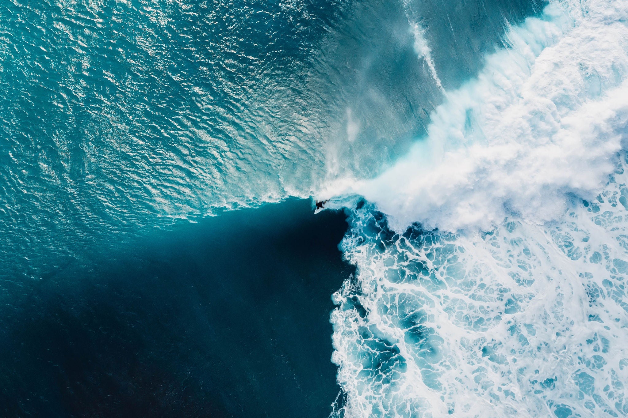 Aerial view with surfers and wave in crystal blue ocean.