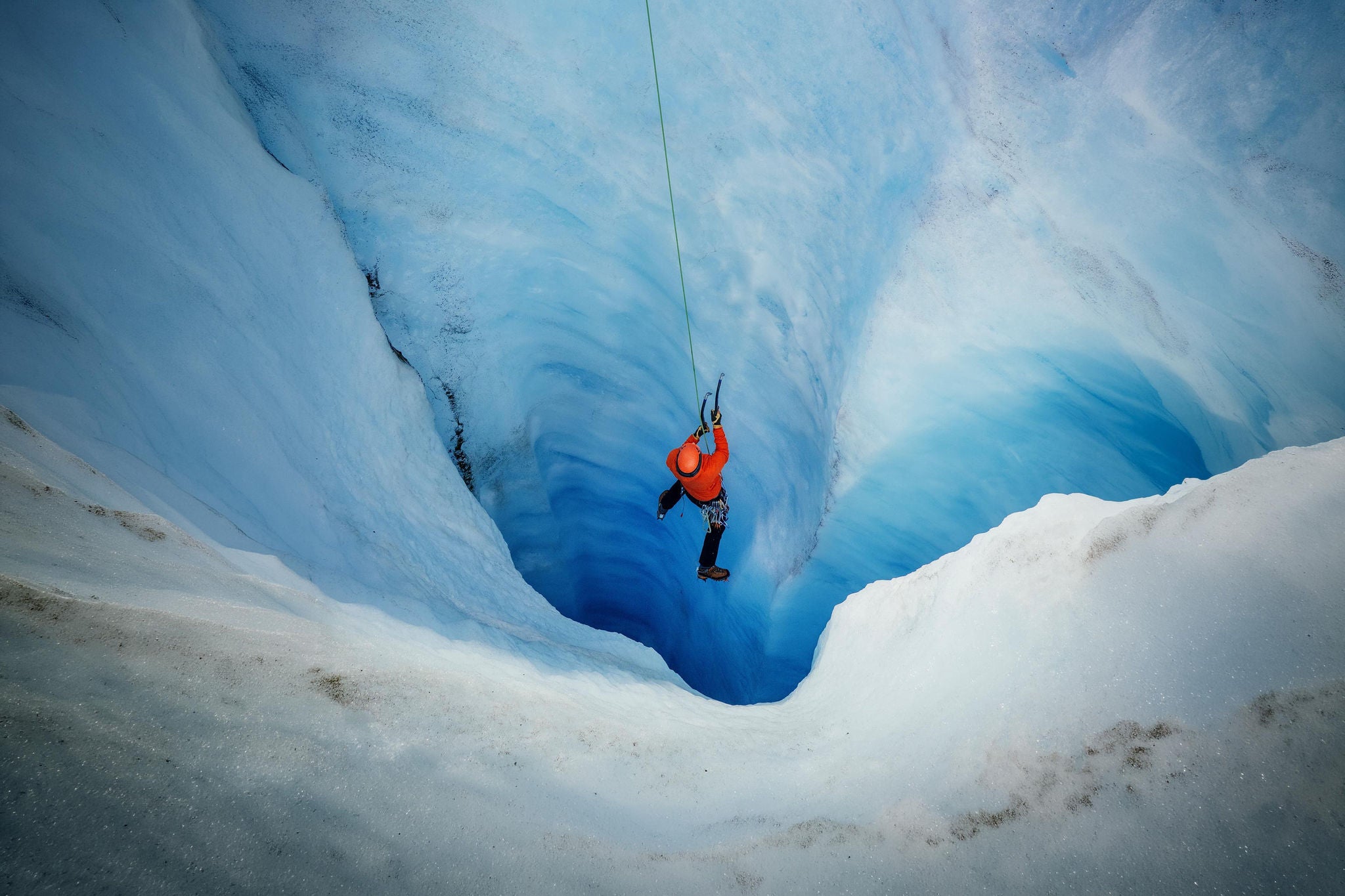 Man in red jacket ice climbing turquoise coloured ice on the Athabasca Glacier
