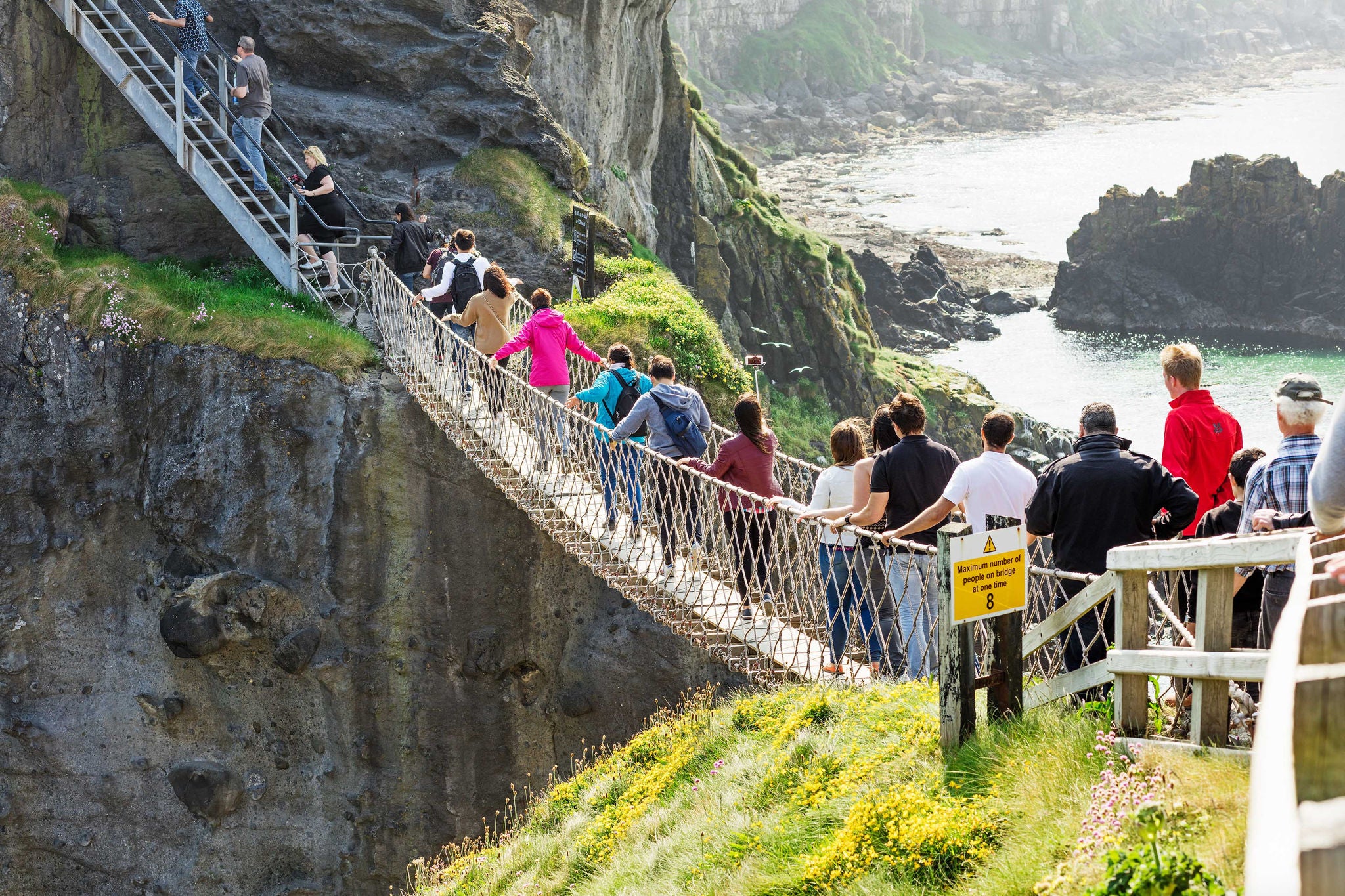 Mensen steken een touwbrug over langs steile kliffen boven de zee bij Carrick-a-Rede.