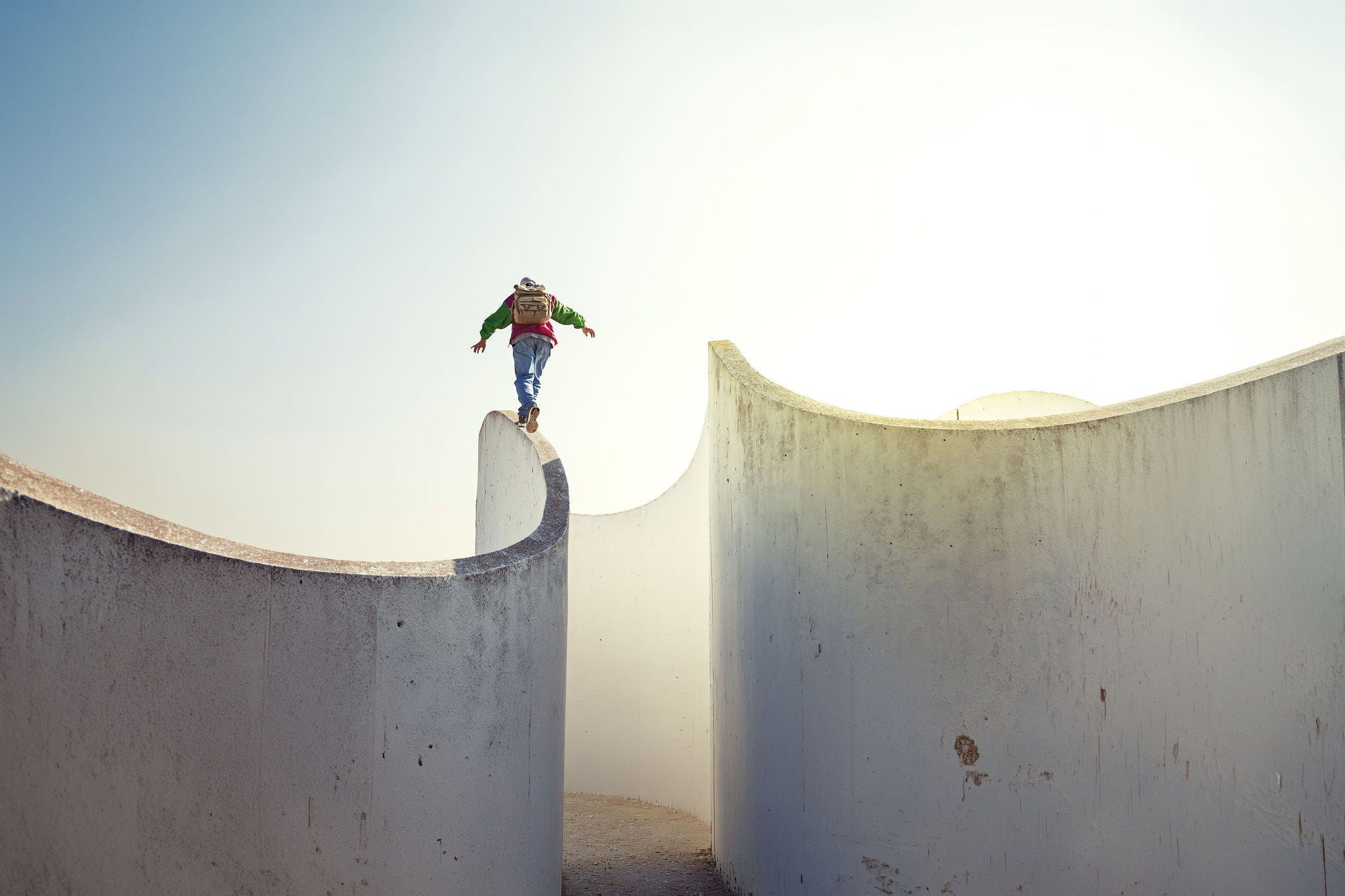 Man with backpack walking on a thin concrete wall 
