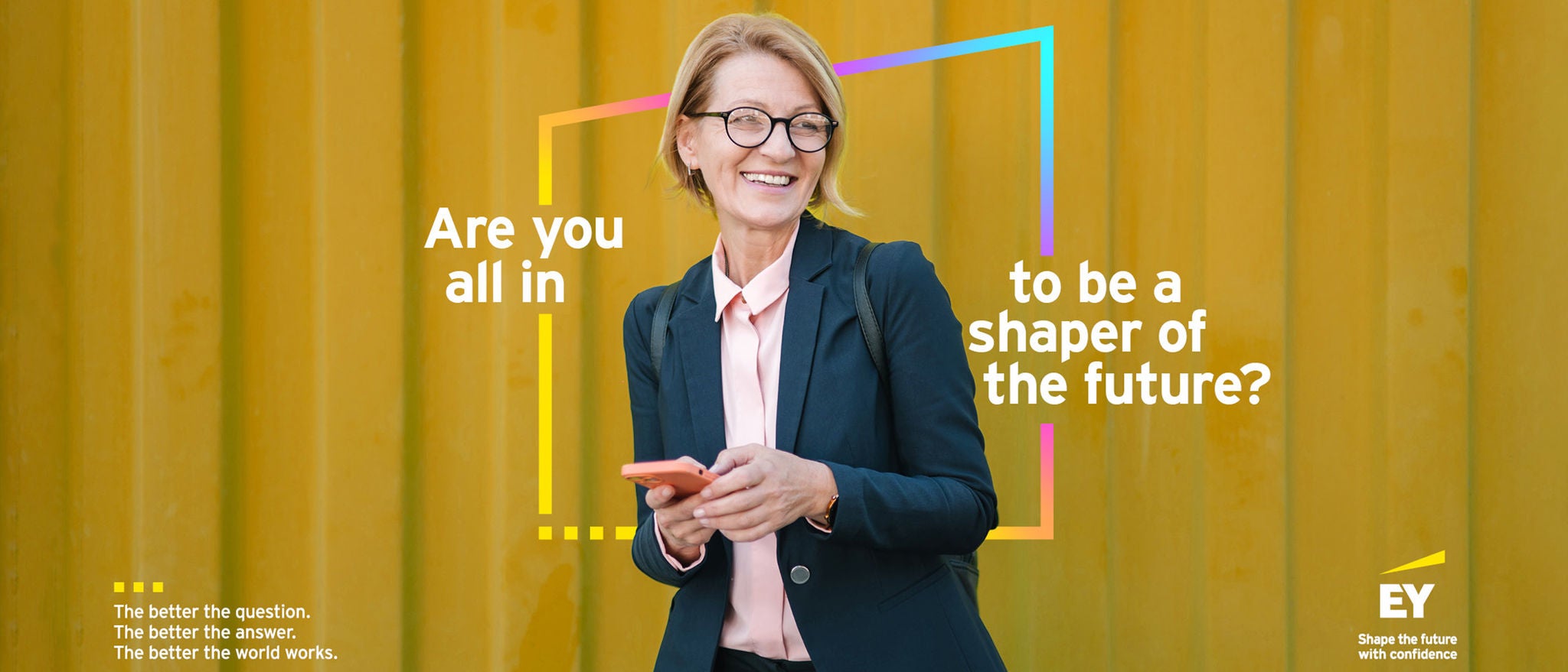 Individual holding a phone before yellow wall with EY message on shaping the future