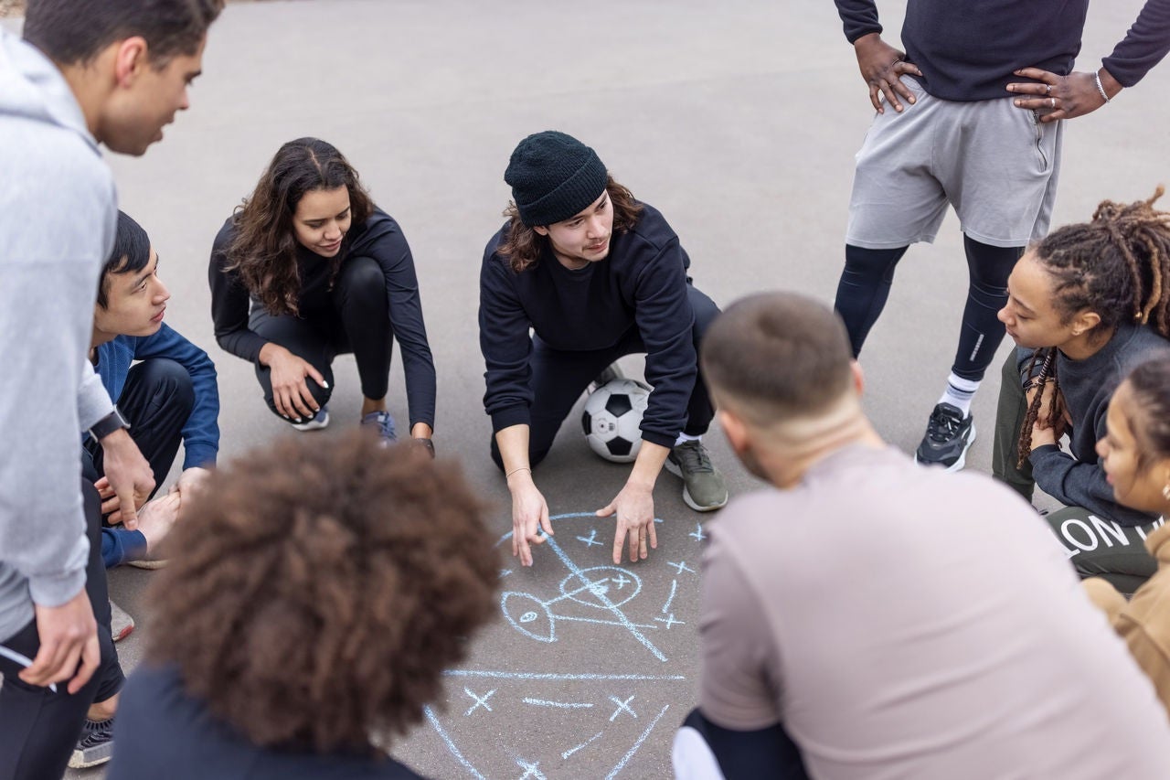 Gruppe analysiert mit Kreide gezeichnete Fussballtaktik auf dem Boden vor dem Training