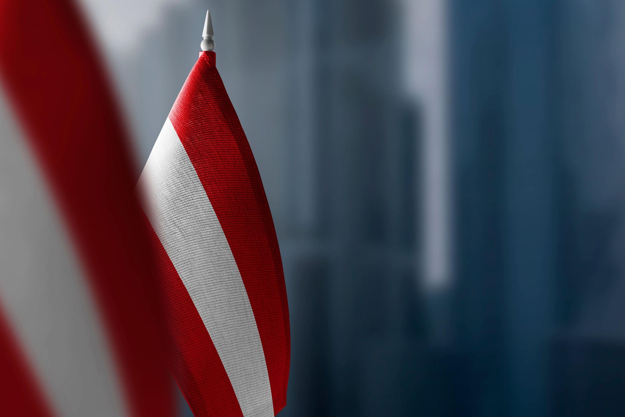 A smiling young woman with headphones and folders, standing outdoors on a college campus.
