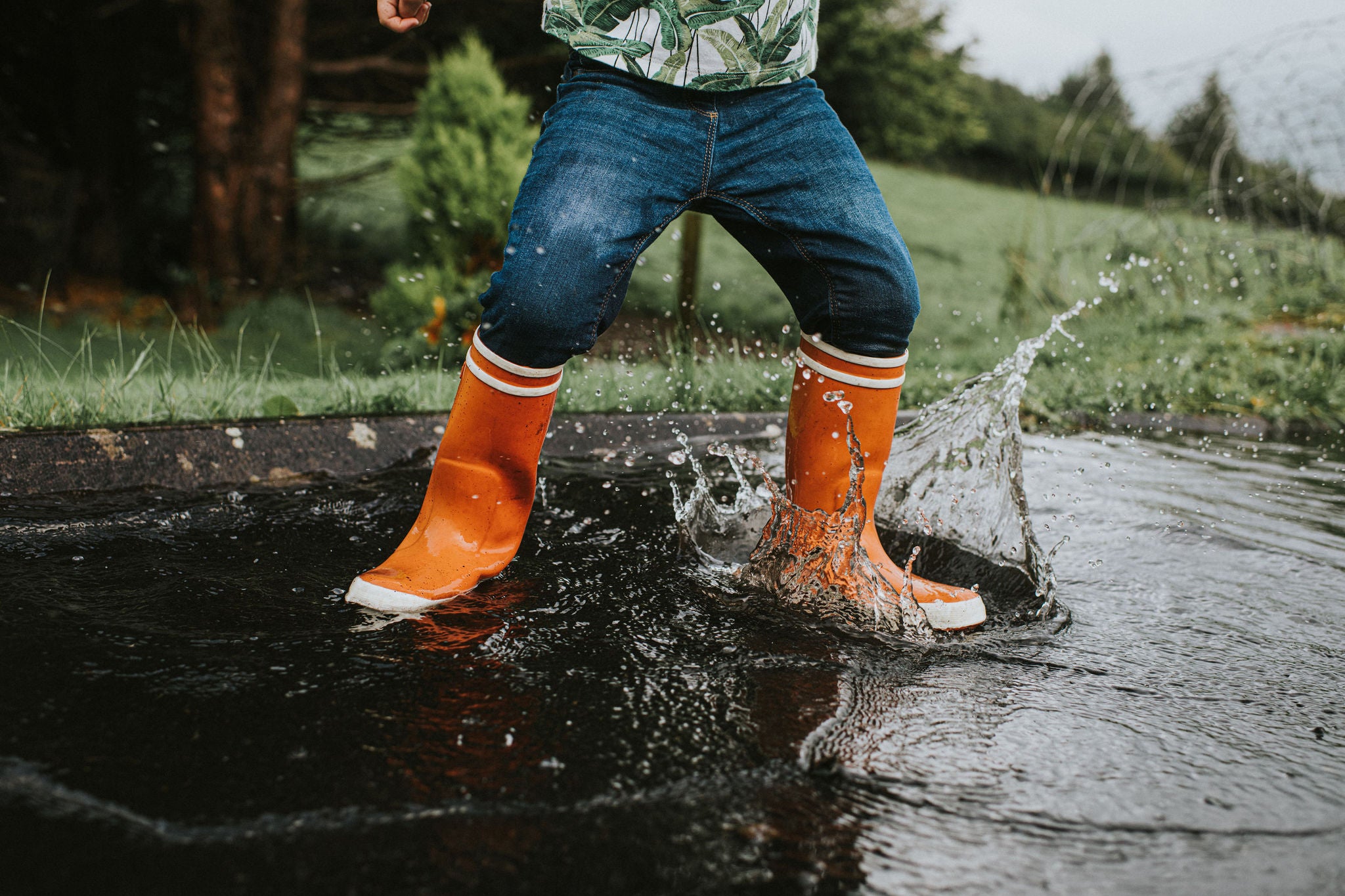 Child wearing orange wellies jumping in a deep puddle