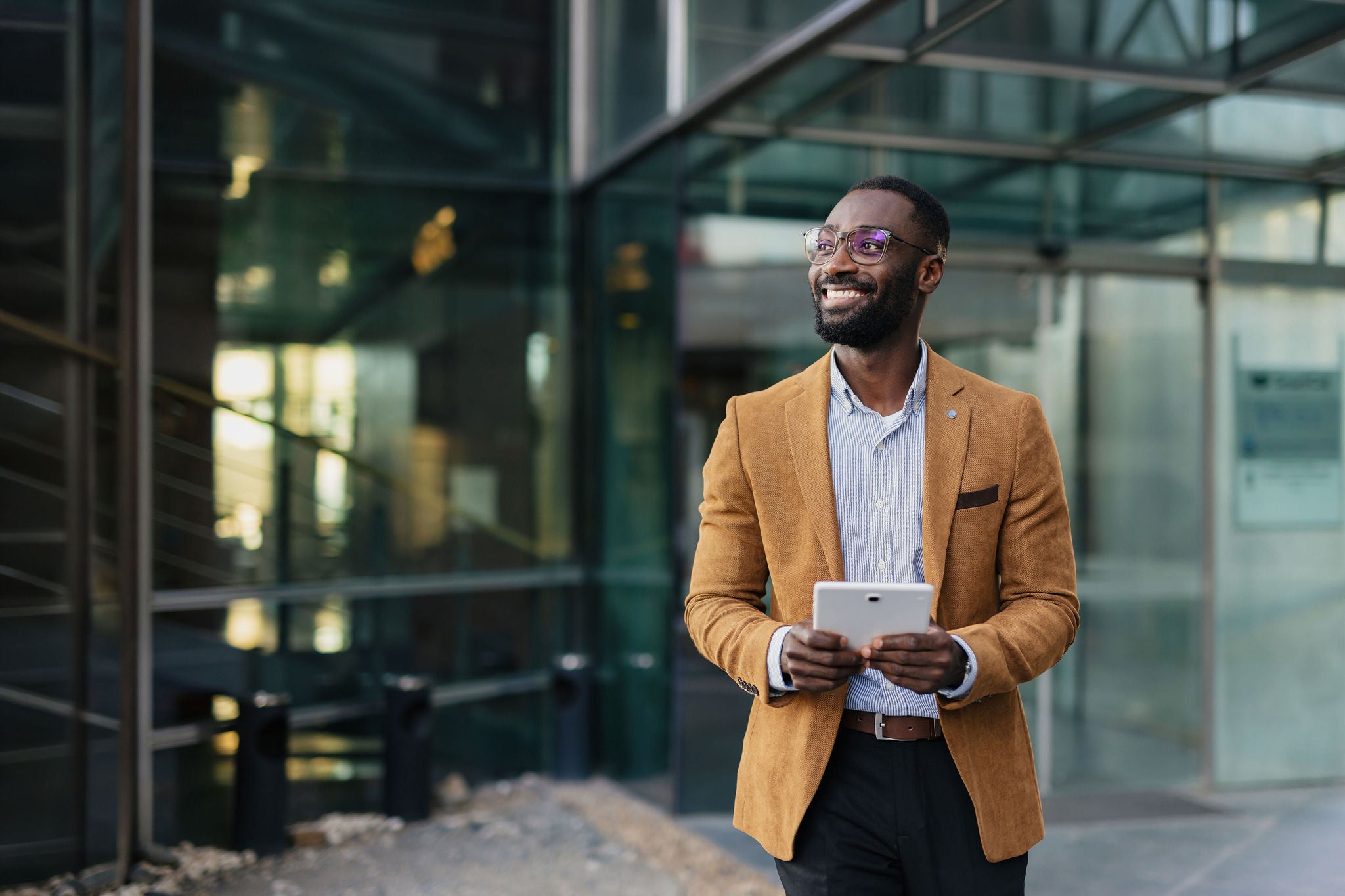 Businessman wearing glasses and a stylish jacket, confidently smiling while holding a tablet