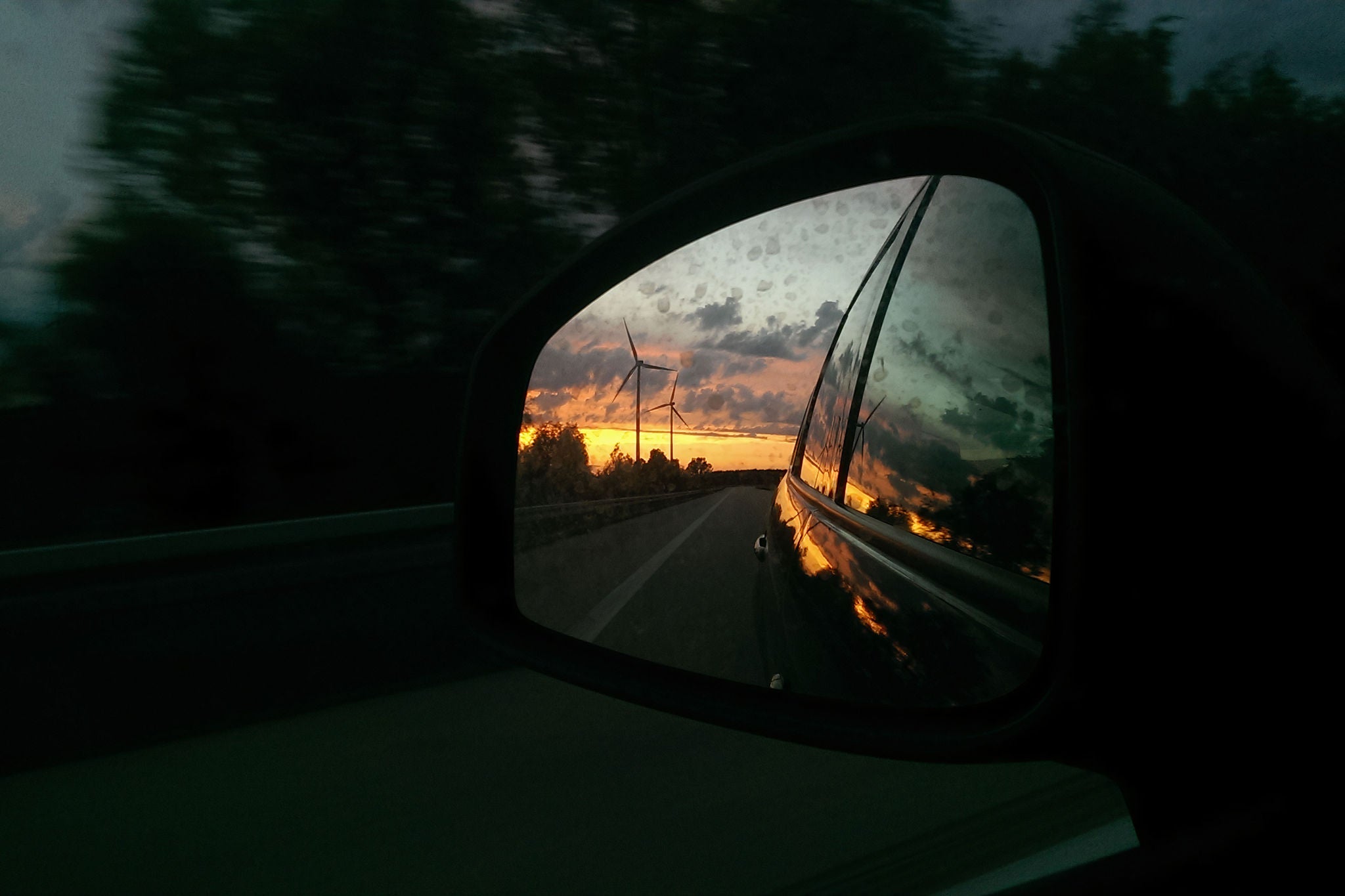 reflection of wind turbines at sunset in car side mirror