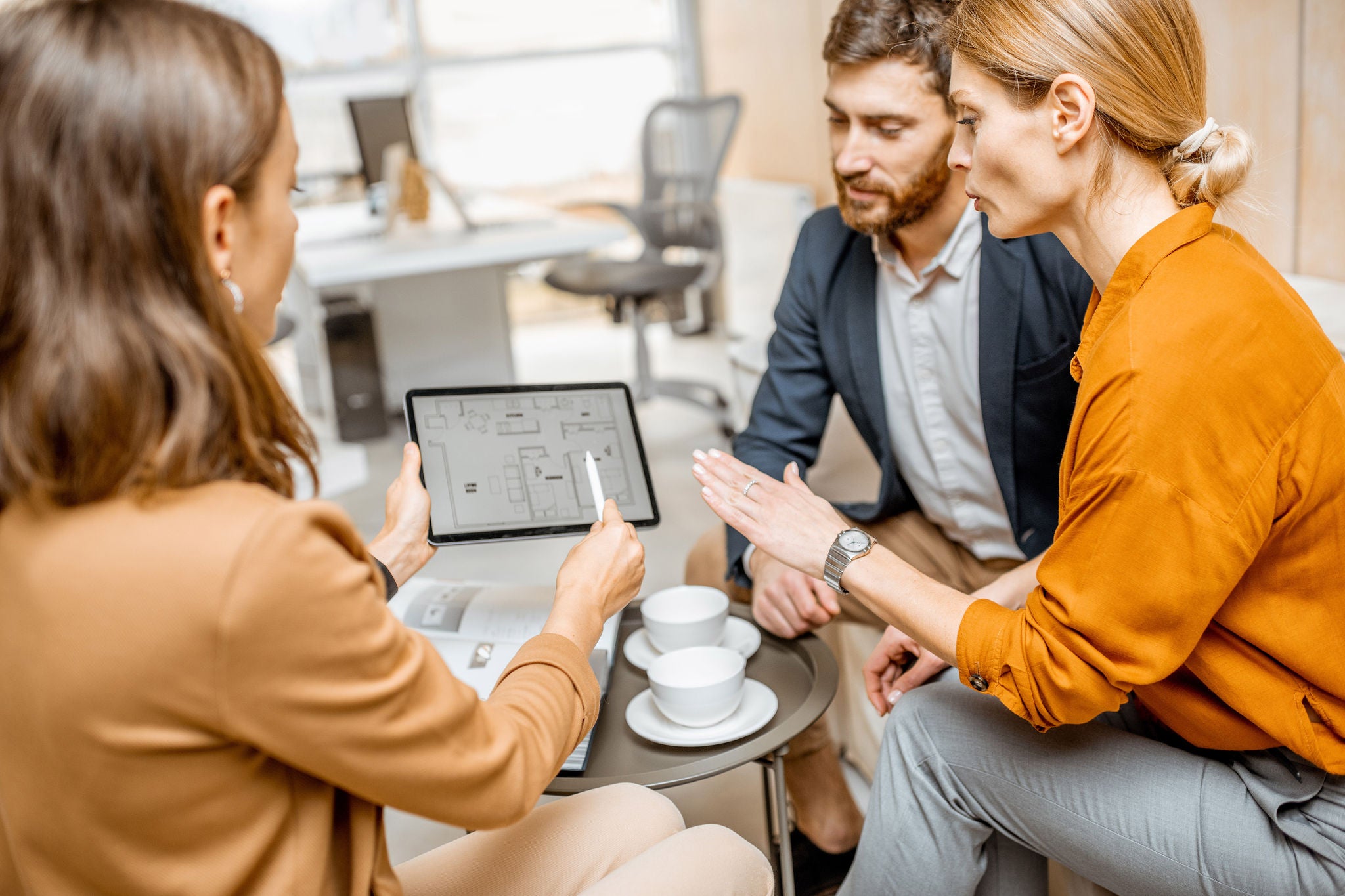 Professionals collaborate around a tablet discussing project plans in a modern office setting.