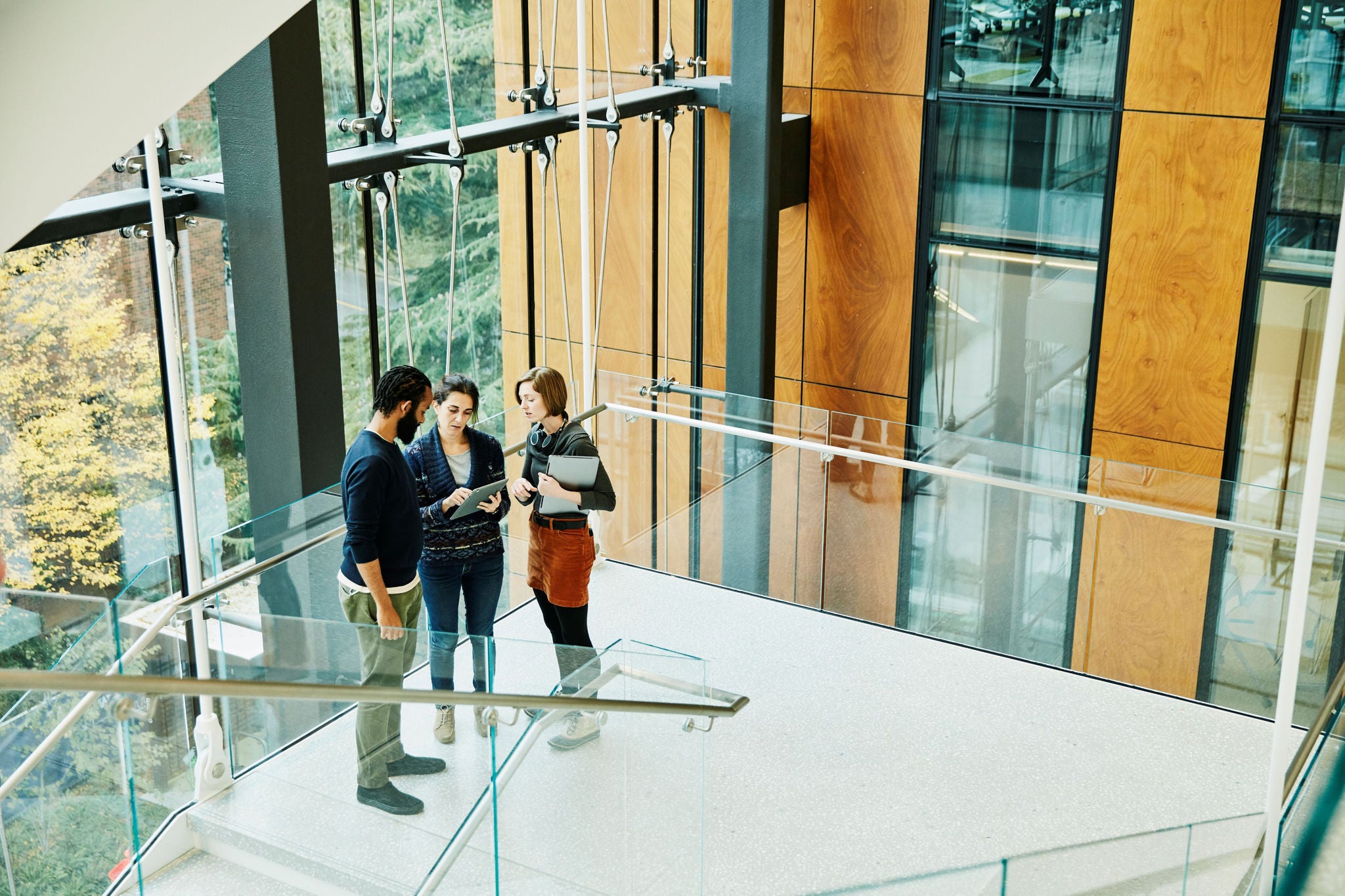 Üvegfalú lépcsőkorlát fordulójában 3 kolléga beszélget.