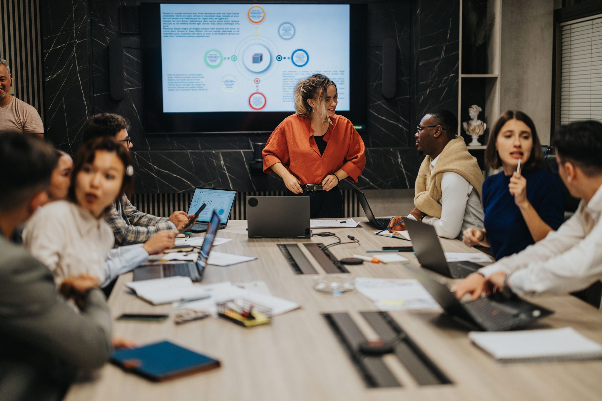 A multiracial group of business people brainstorm solutions in a modern office. The team engages in discussion, utilizing technology to strategize and plan for business growth. Collaboration is key.