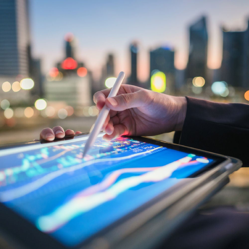 Eine Hand benutzt einen Stift auf einem Tablet, das dynamische Finanzdiagramme und -grafiken anzeigt.