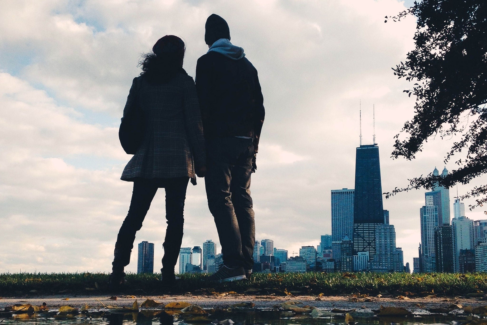 Rear View Of Man And Woman Looking At Cityscape Against Cloudy Sky