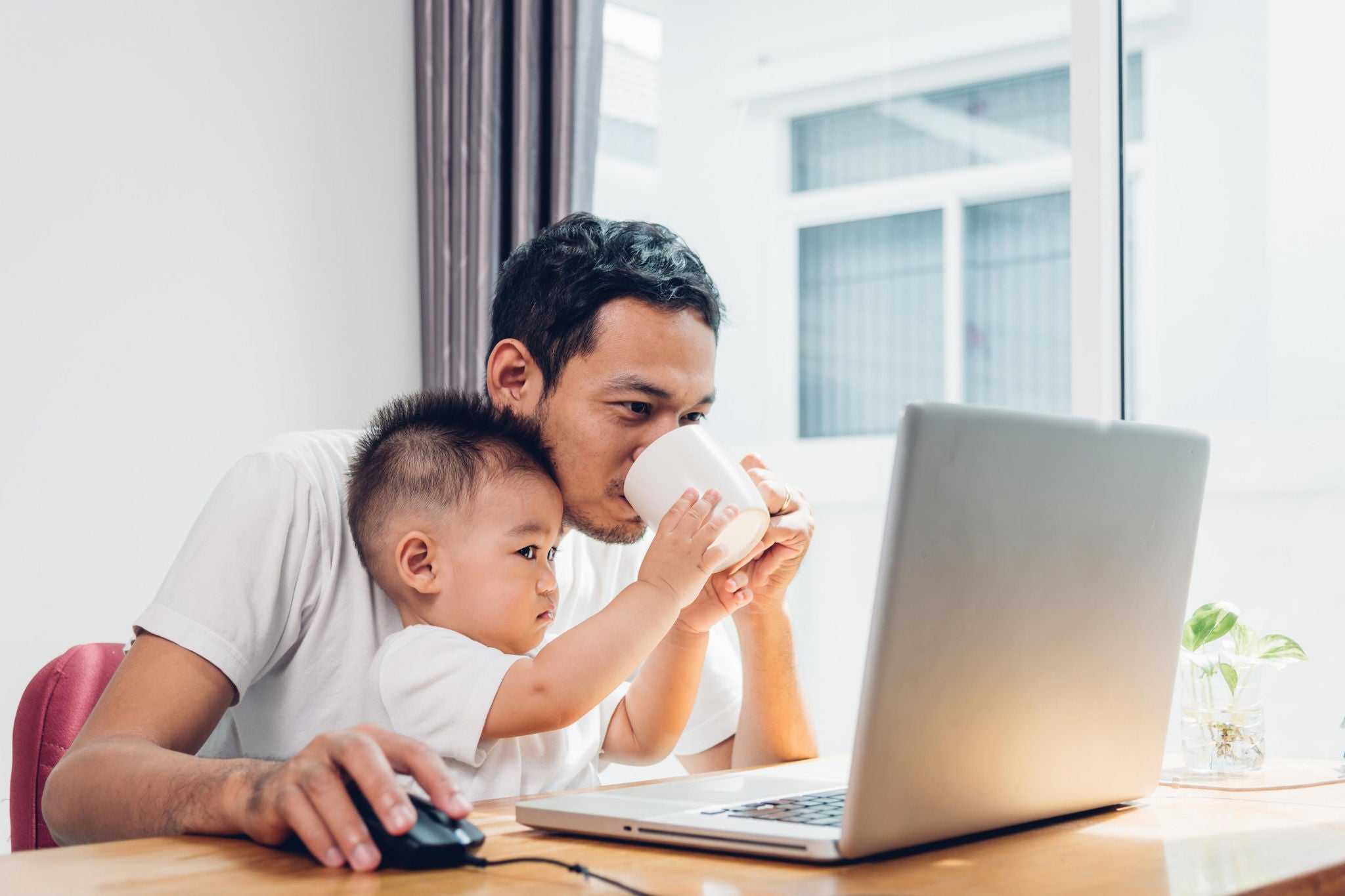 Father holding son while working at laptop