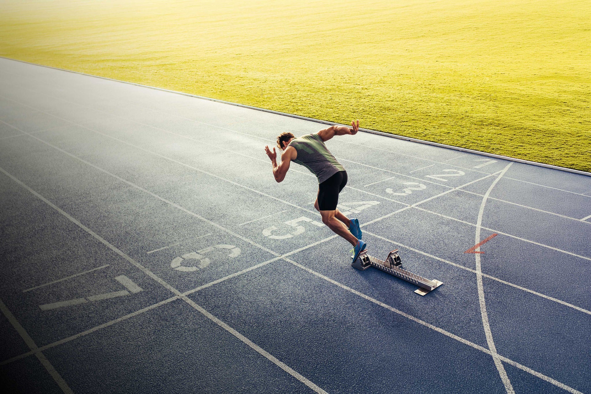 Rear view of an athlete starting his sprint on an all-weather running track. Runner using starting block to start his run on race track.