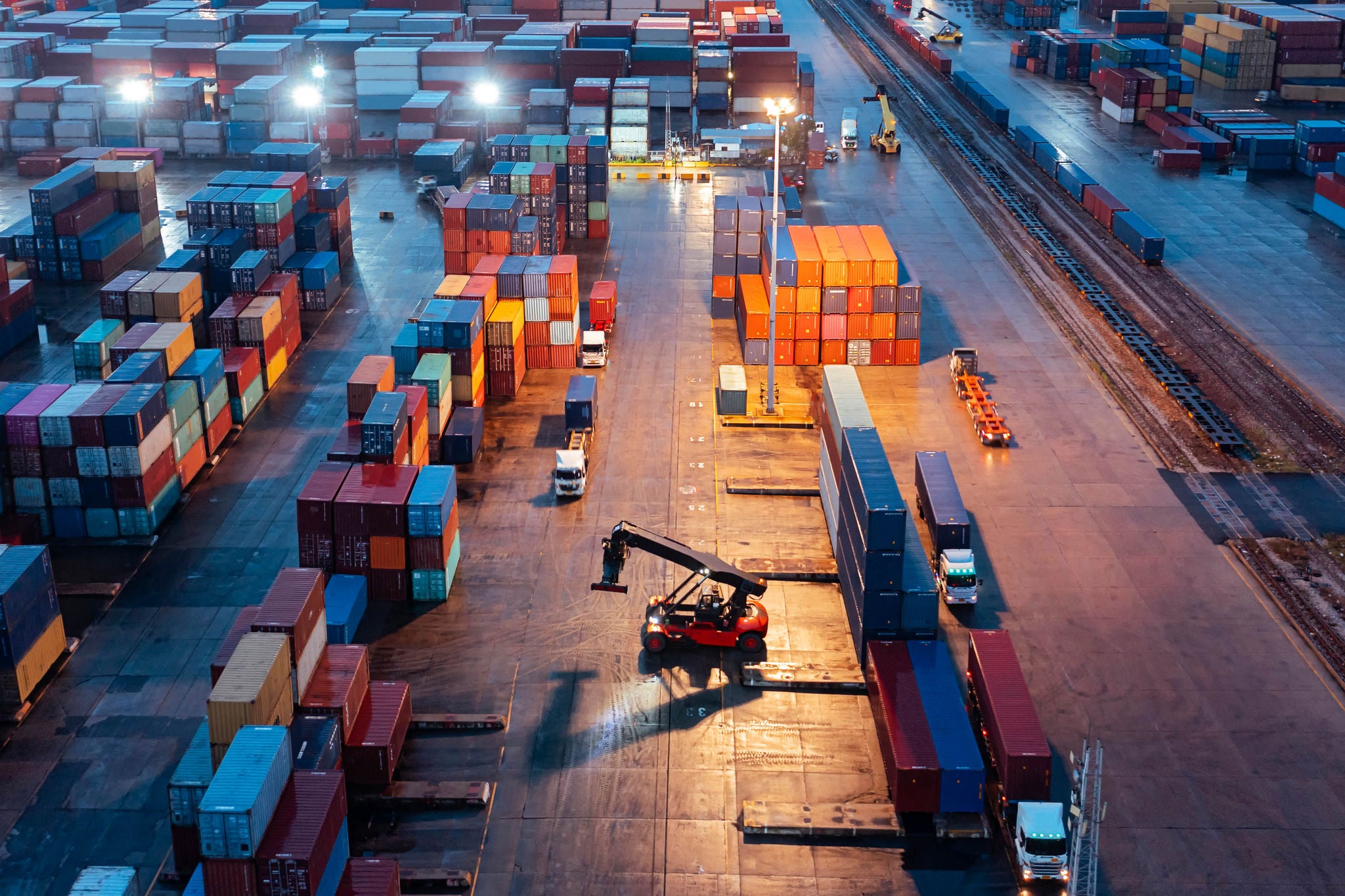 Aerial view of a container yard with stacked containers, trucks and a forklift