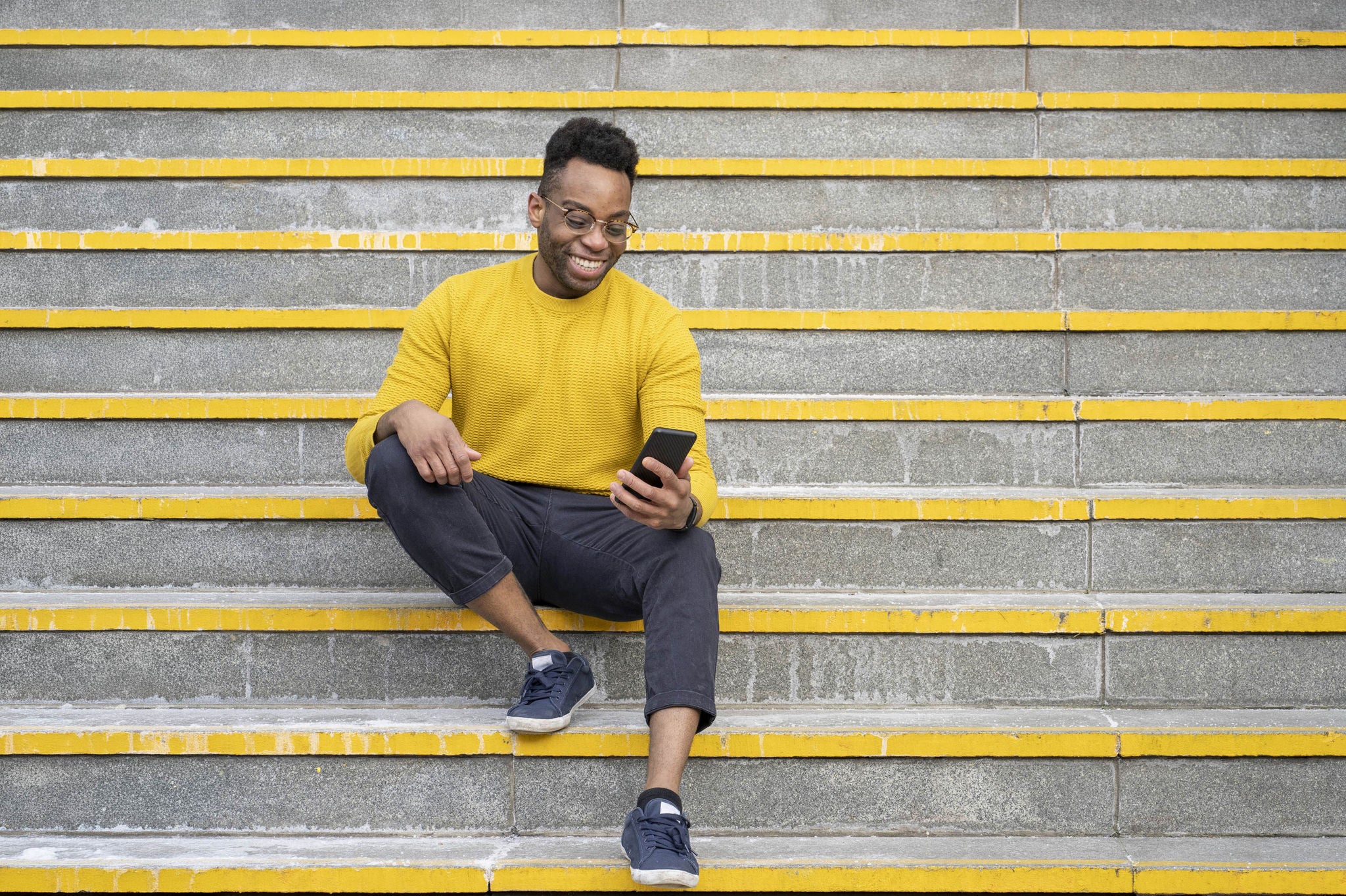 Smiling young man using smart phone while sitting on staircase 