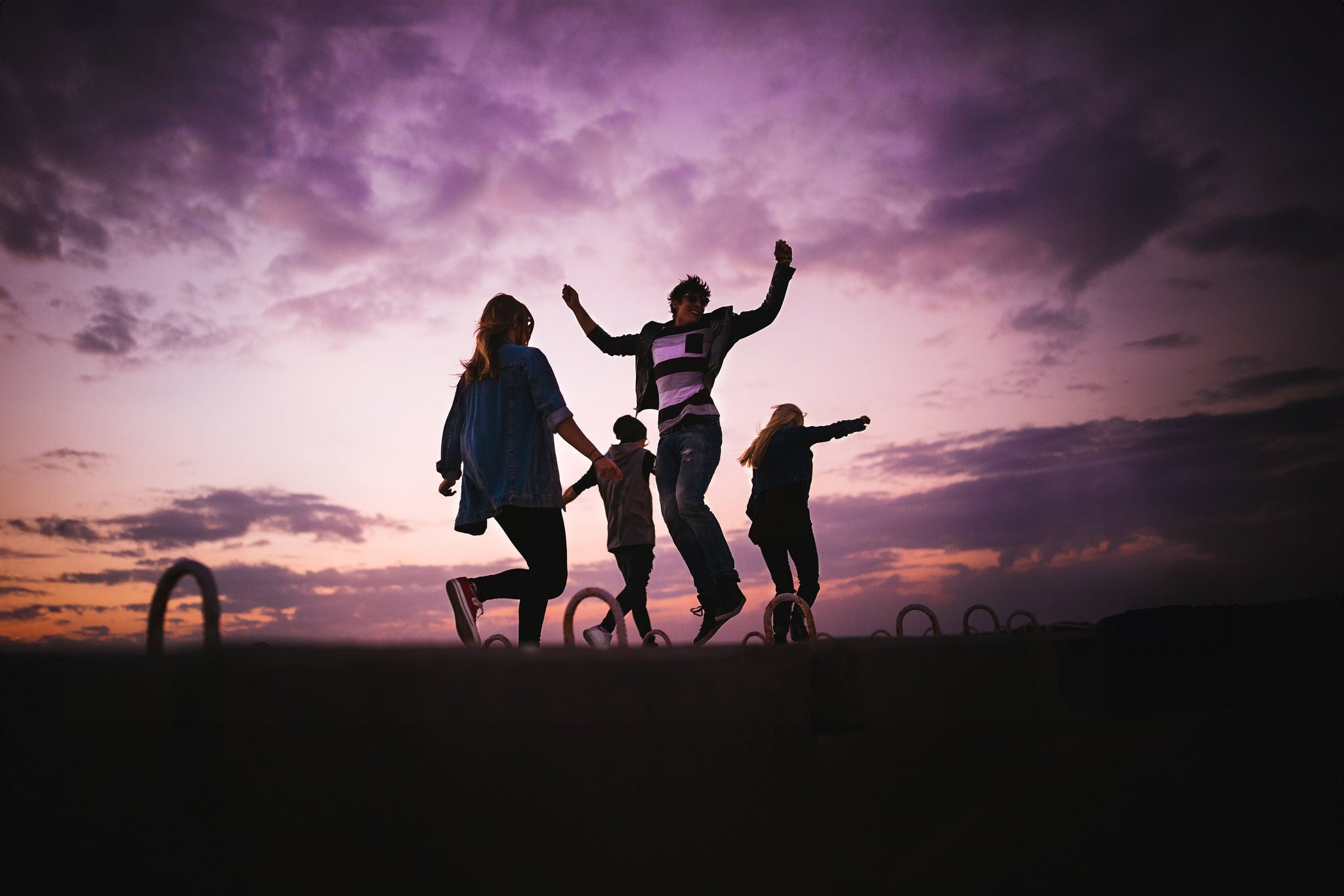 Group of young hipster friends jumping, dancing, having fun and partying outdoors at sunset