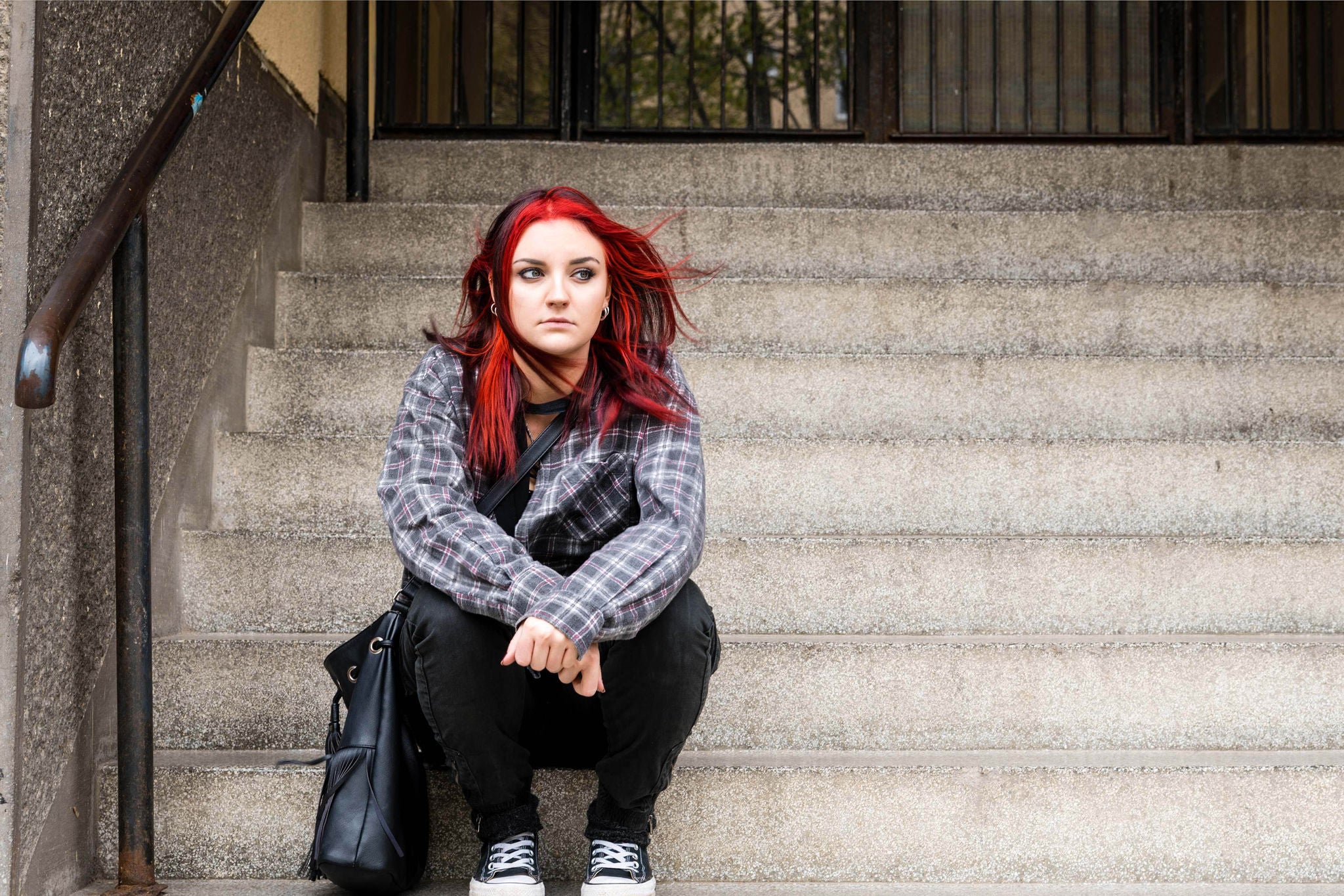 Homeless girl, Young beautiful red hair girl sitting alone outdoors on the stairs of the building with hat and shirt feeling anxious and depressed after she became a homeless person