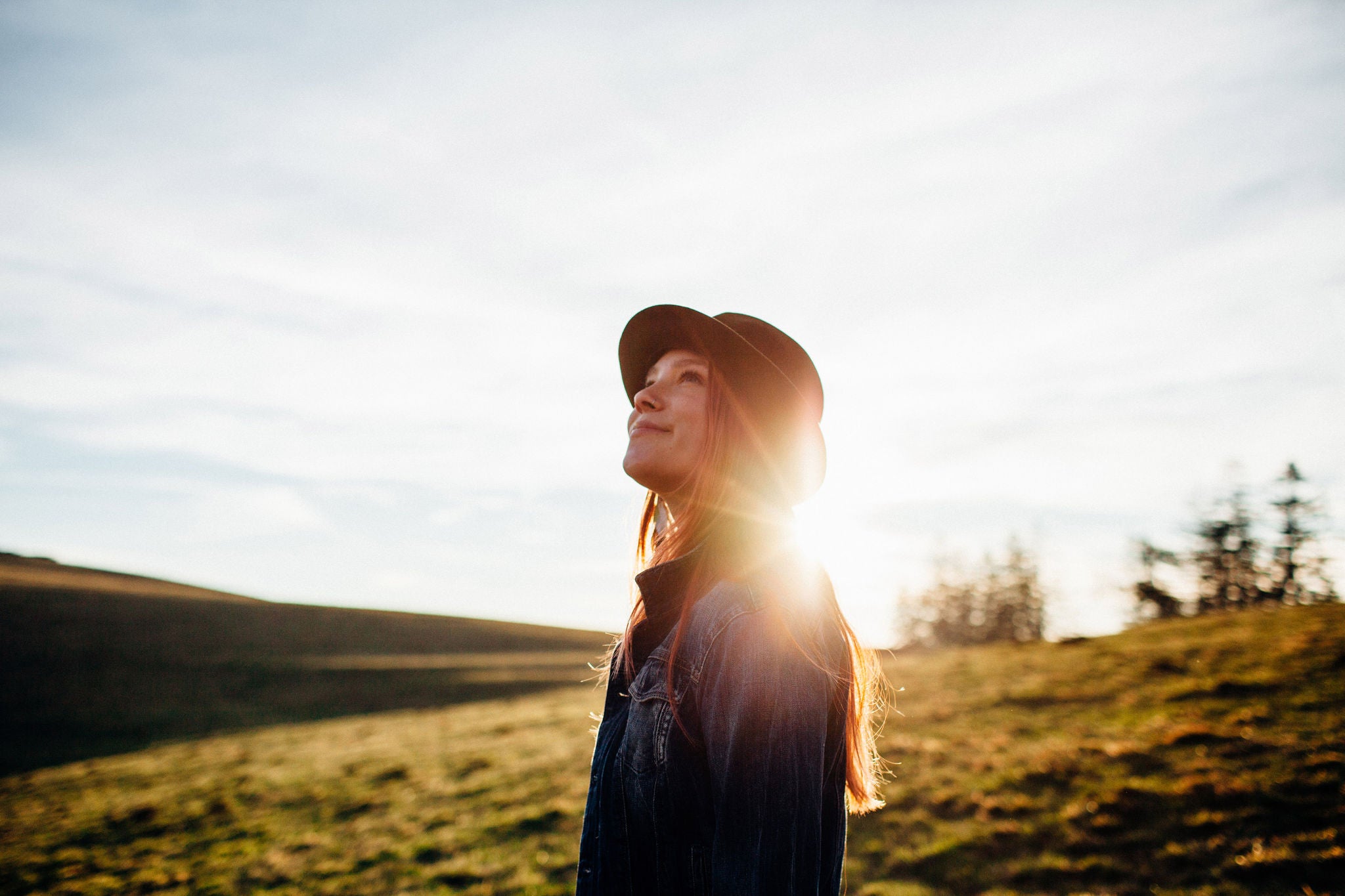 Woman wearing a hat outside with the sunset behind her