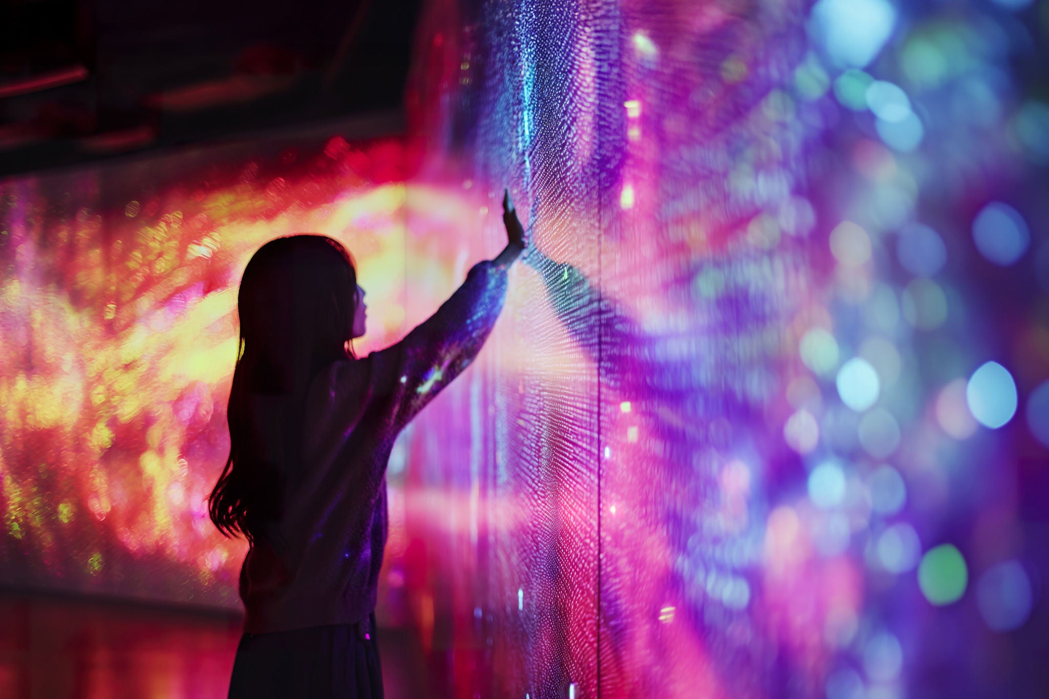 Person berührt eine farbenfrohe digitale Lichtwand und symbolisiert immersive Technologieerlebnisse.