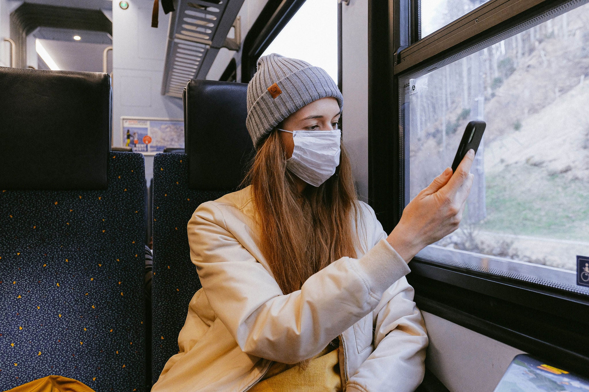 Woman on train in Europe, wearing COVID mask, looking at cell phone, mobile,