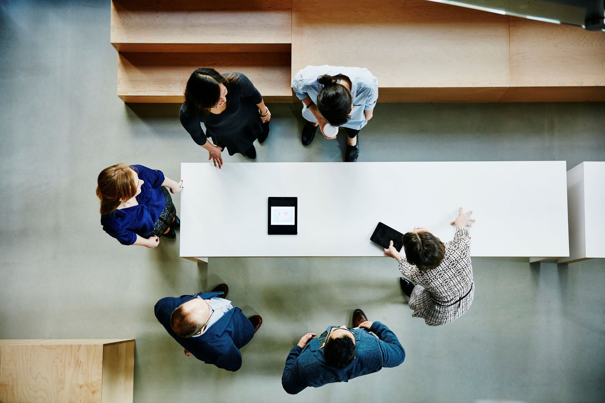 Overhead view of a group gathered around a white table with tablets in a modern office.