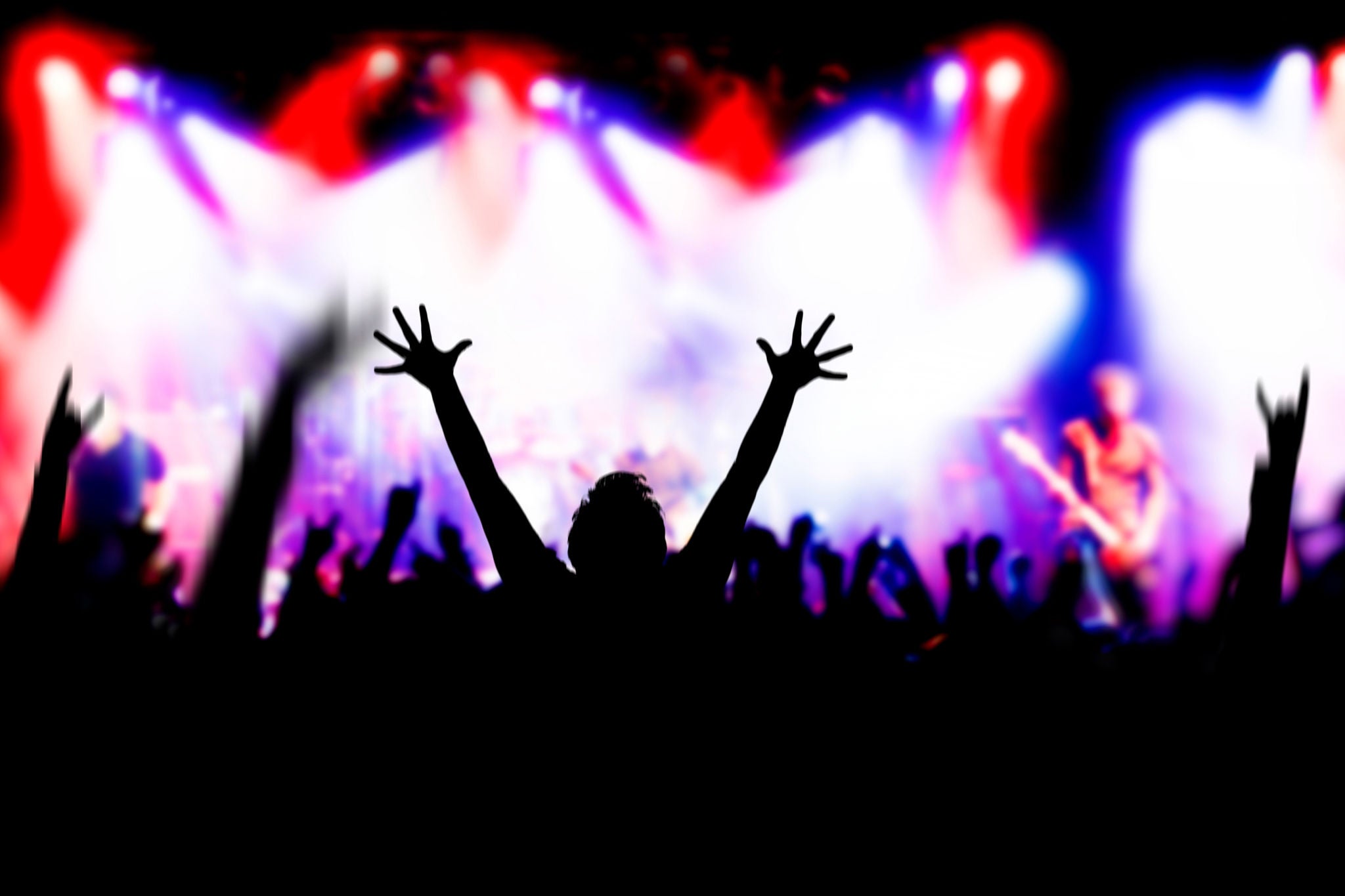 Fans raising hands in excitement at a rock concert, some blur and noise because of low light and fast movement