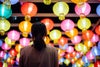 Rear view of young Asian woman looking up and admiring the hanging illuminated and colourful traditional Chinese lanterns on city street at night. Traditional Chinese culture, festival and celebration event theme