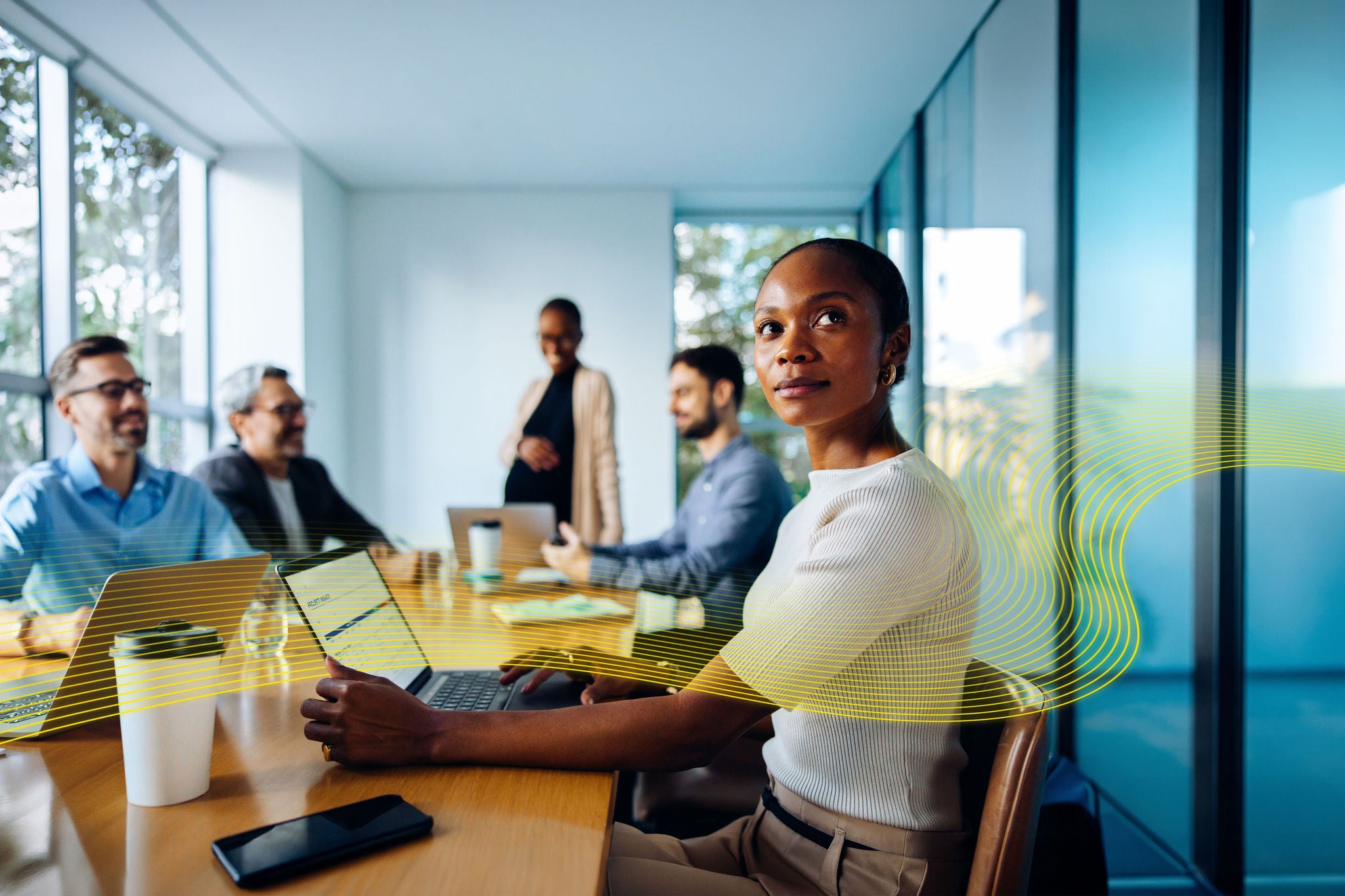 A diverse team of young professionals discussing business strategies around a conference table equipped with laptops and documents in an office meeting room.