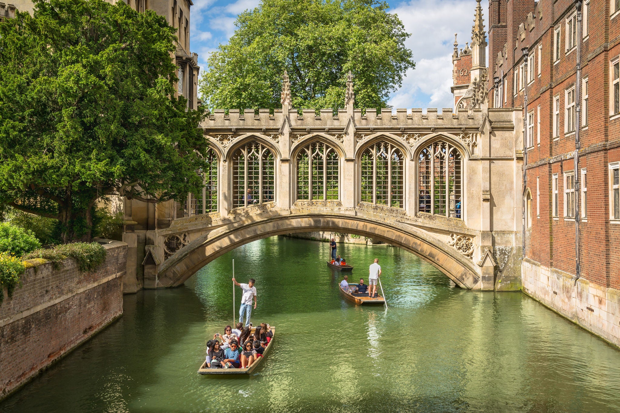 People punting along a river beneath an arched stone bridge