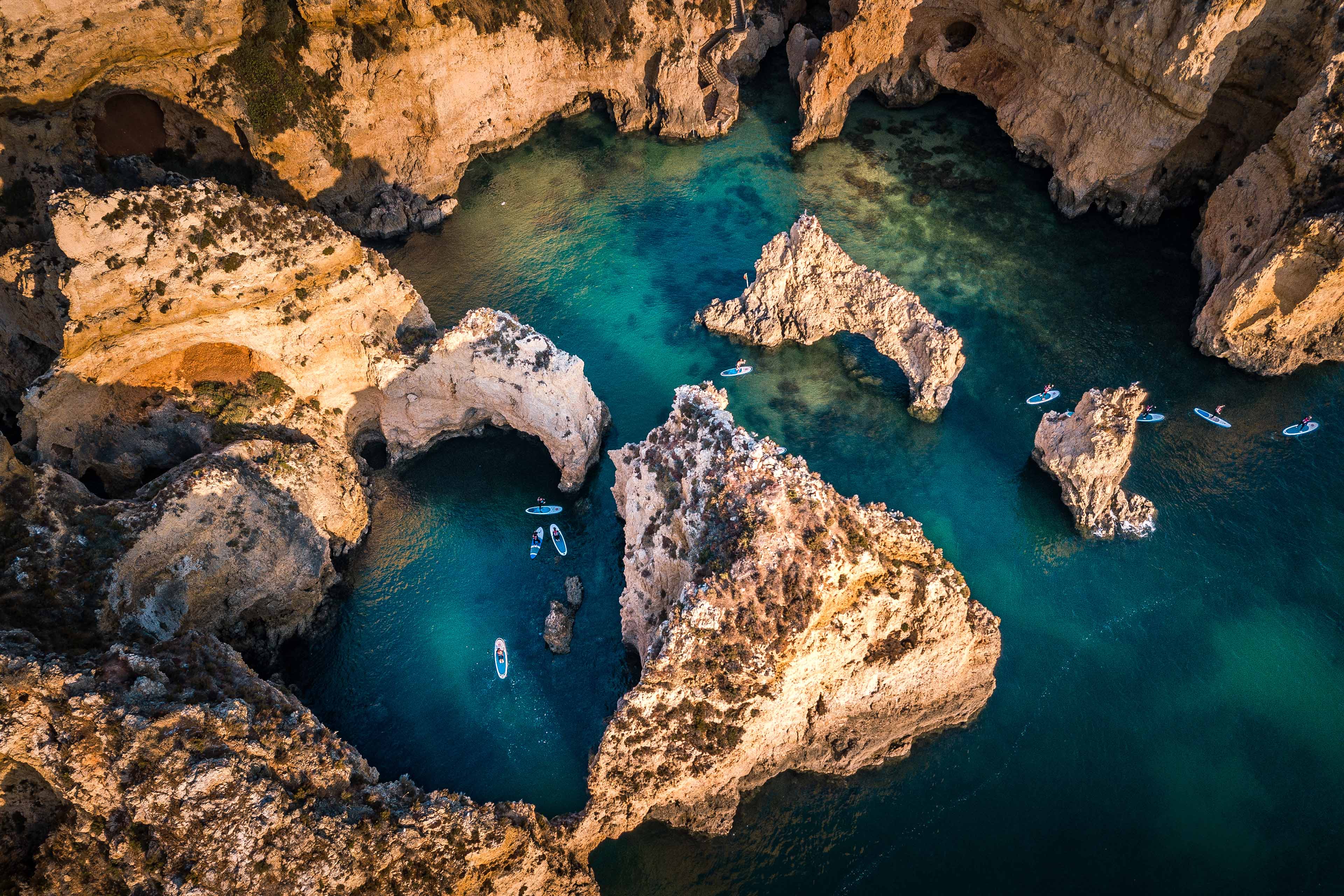 Aerial view of rocky sea caves and turquoise water with paddleboarders.