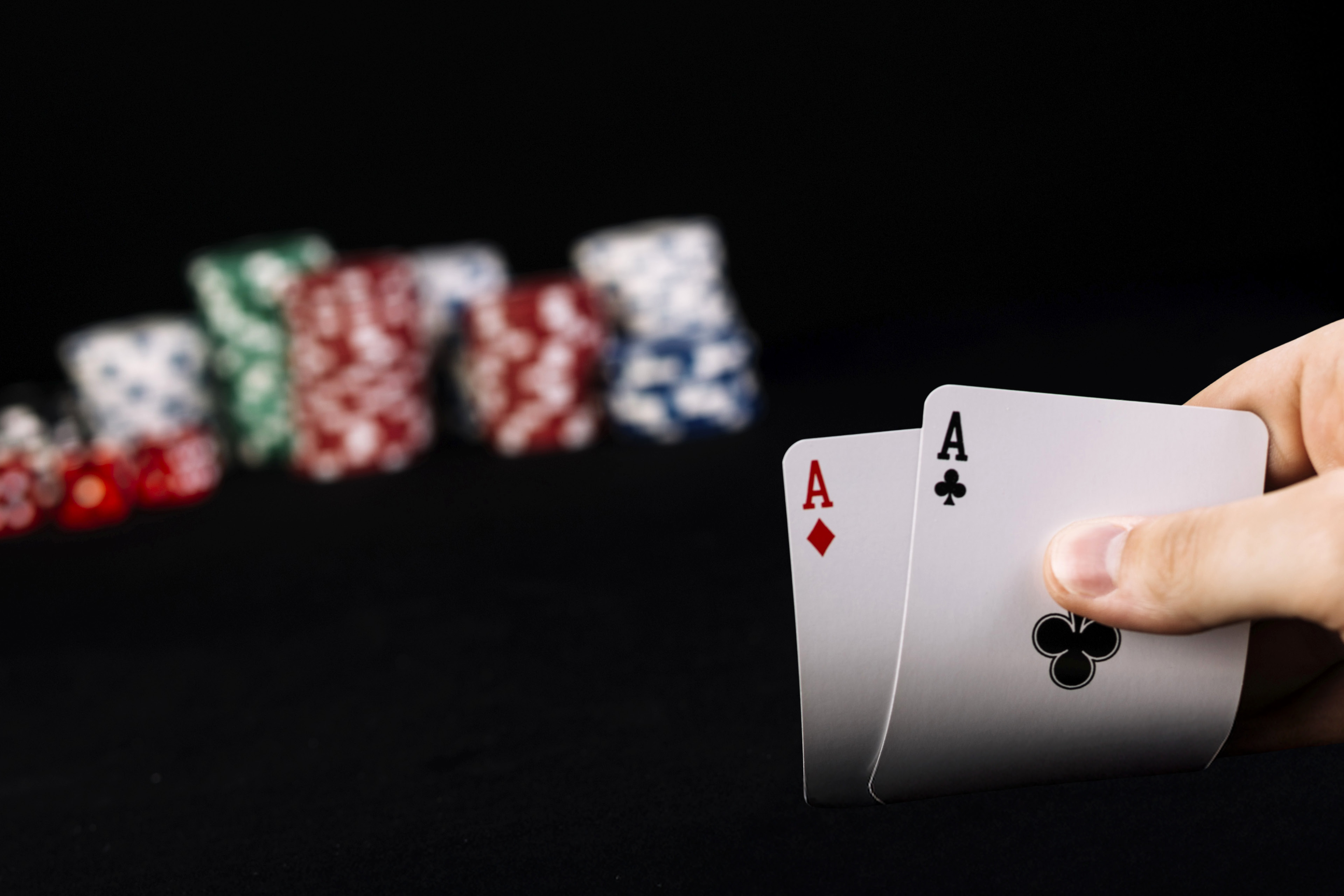 Nahaufnahme der Hand eines Spielers, der zwei Asse in der Hand hält, mit Pokerchips im Hintergrund.