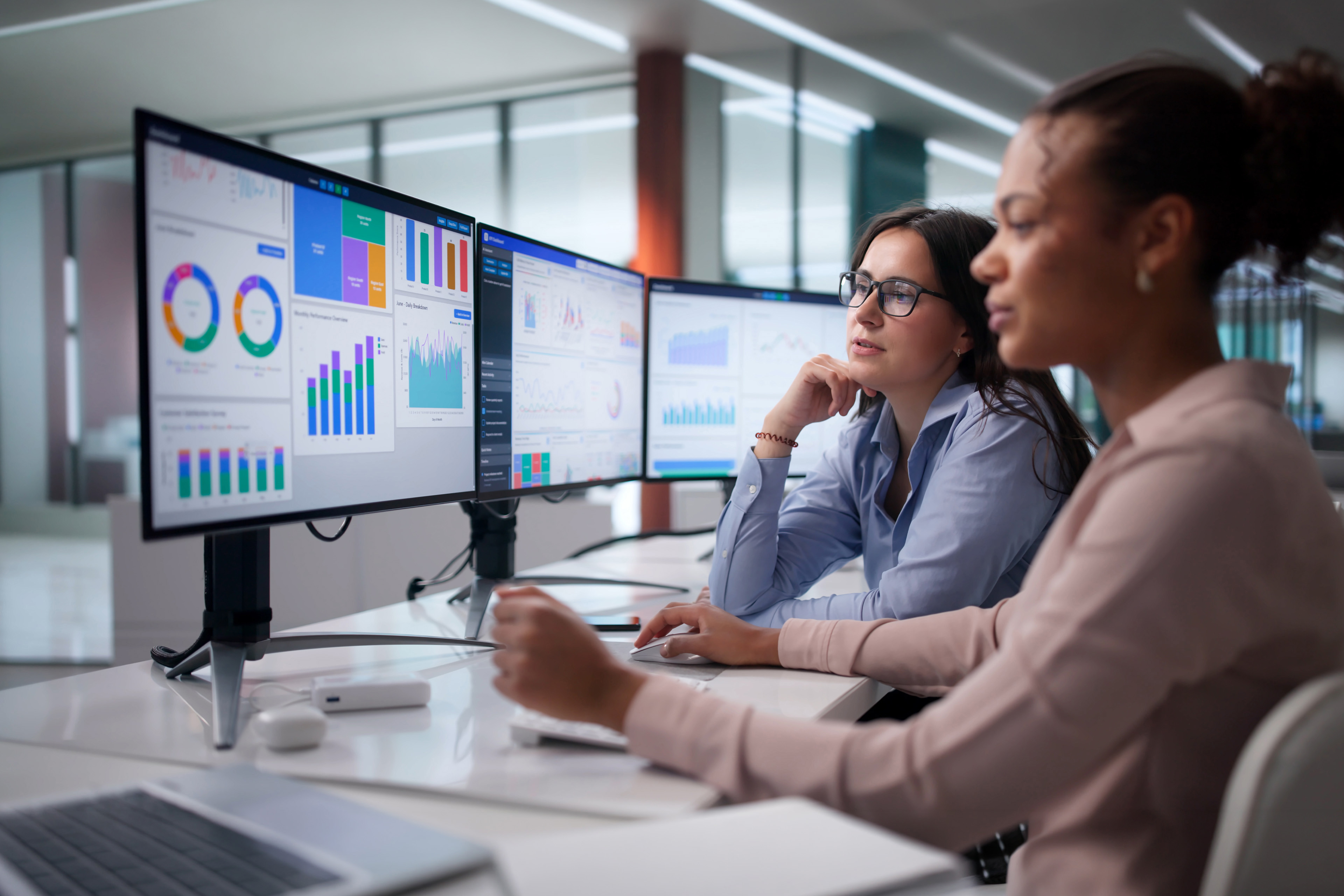 Fachkräfte analysieren Dashboards und Berichte auf mehreren Bildschirmen in einem modernen Büro.