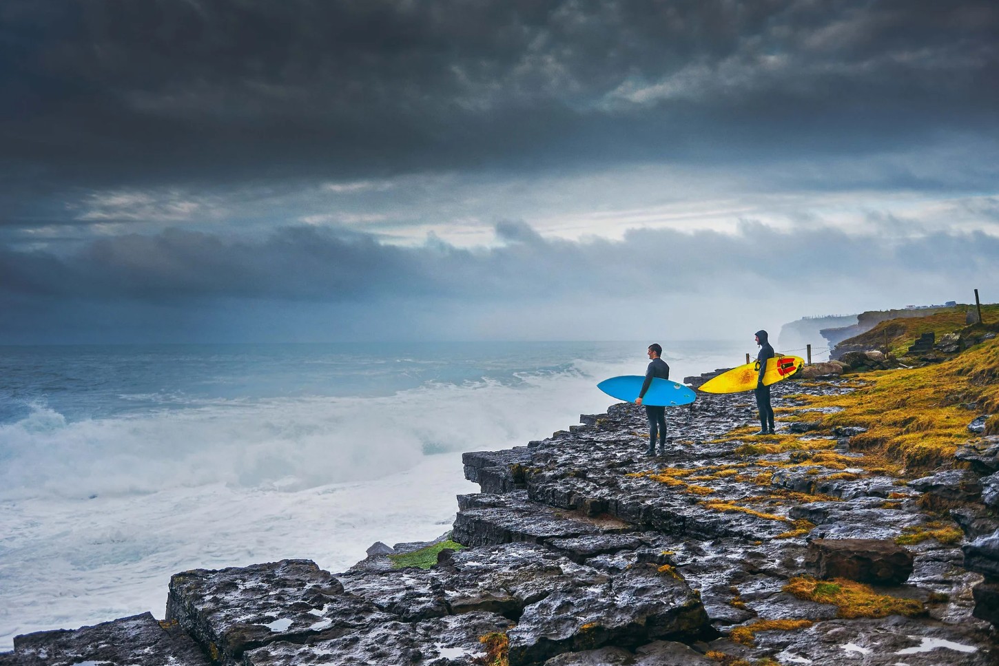 two surfers at a rocky cloudy beach