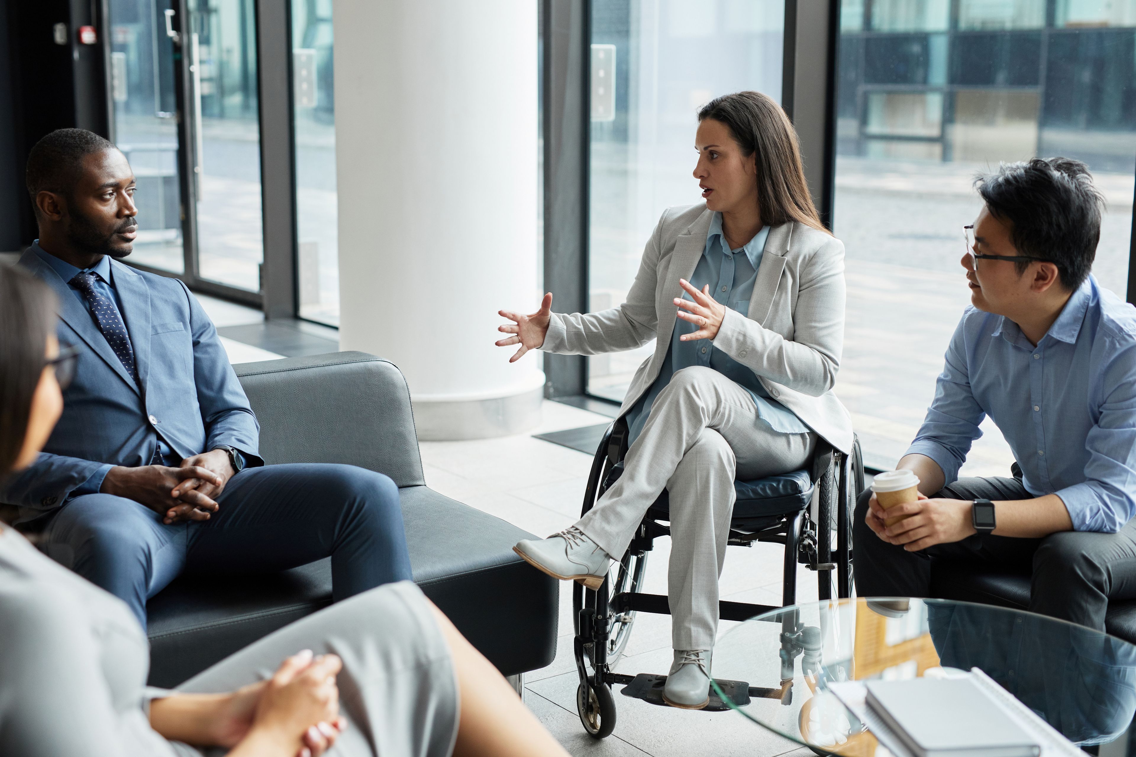 Business woman using wheelchair sitting among group of colleagues