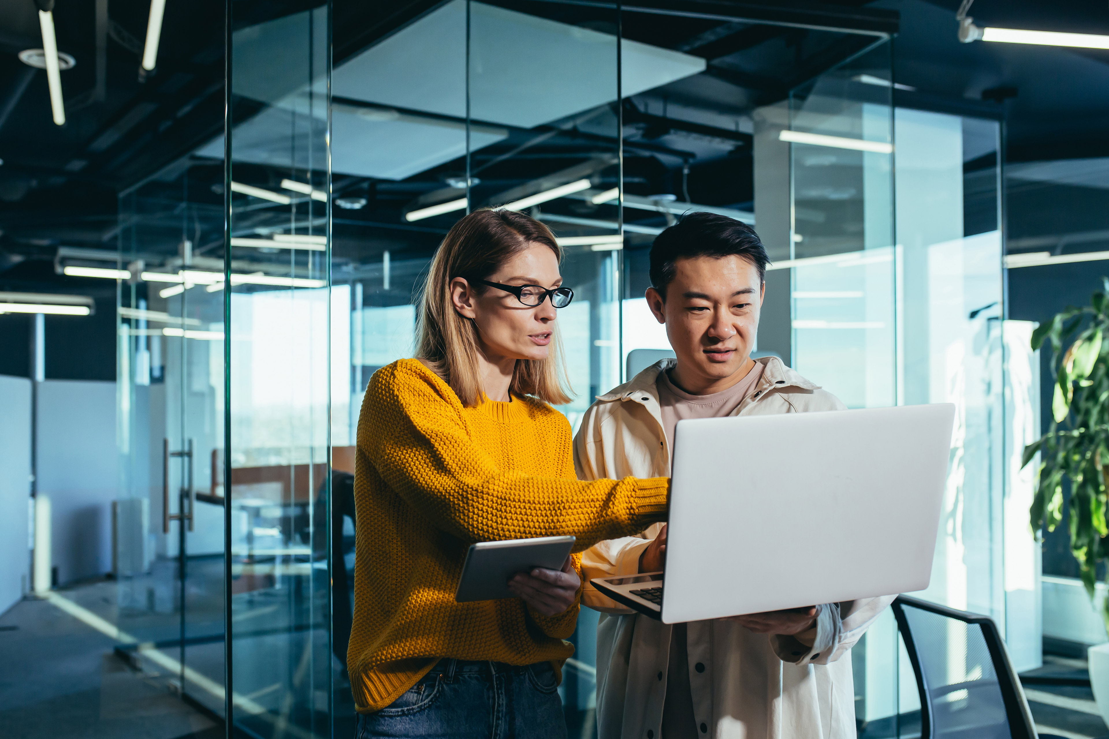 Two people working together on a laptop in a modern office with glass walls