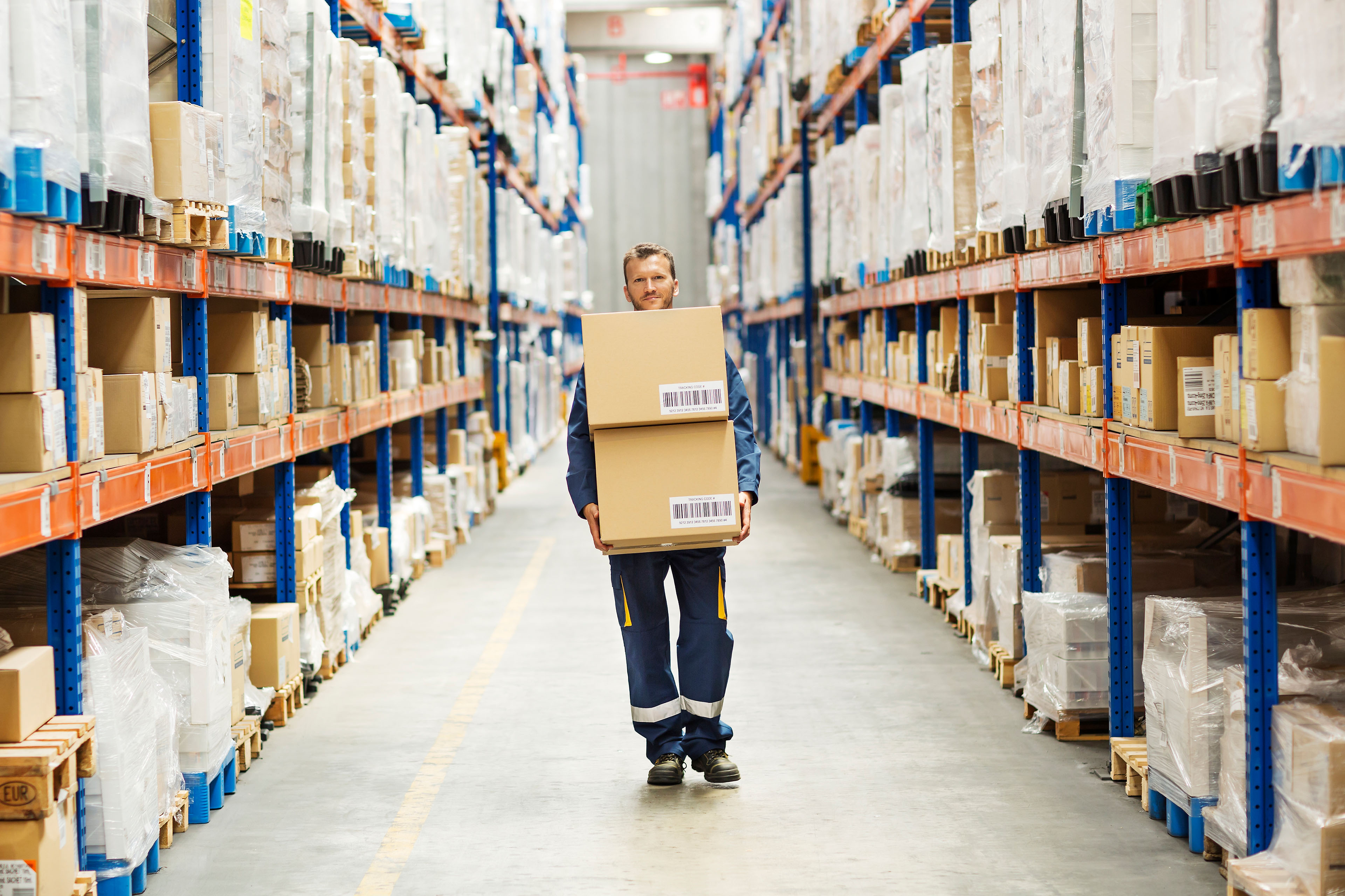 Worker carrying boxes in a warehouse aisle