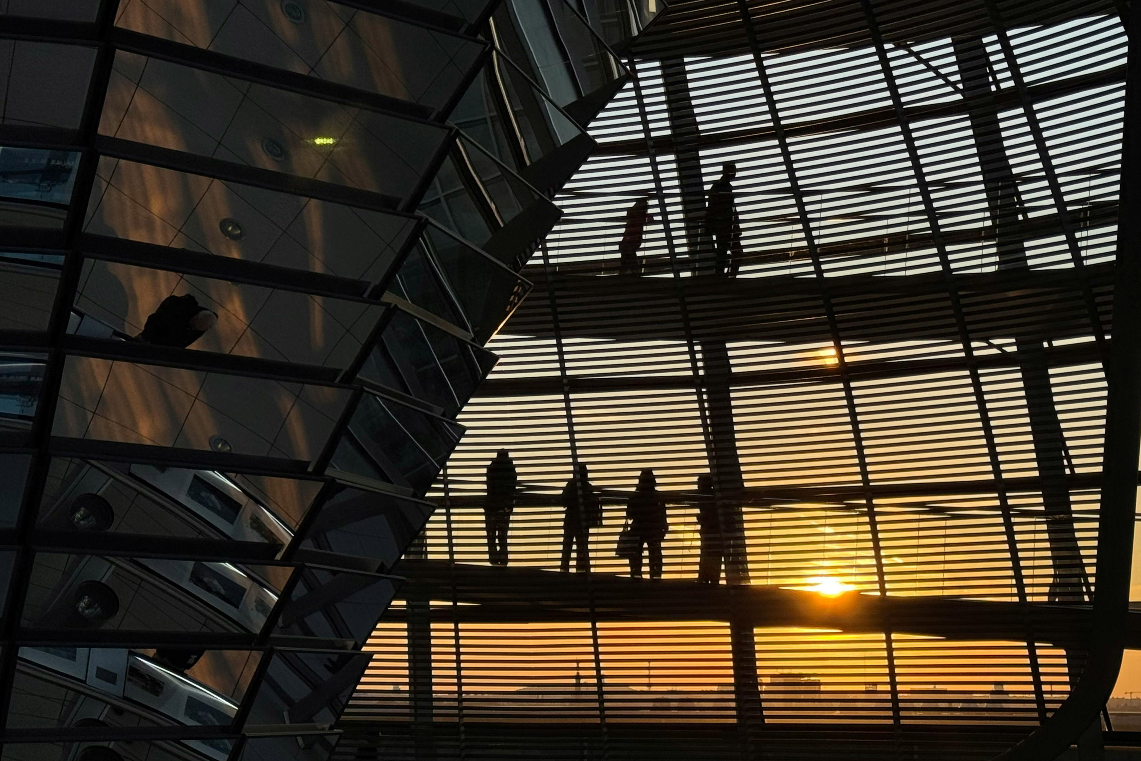 Silhouettes of people walking inside a modern office building with large glass windows at sunset.