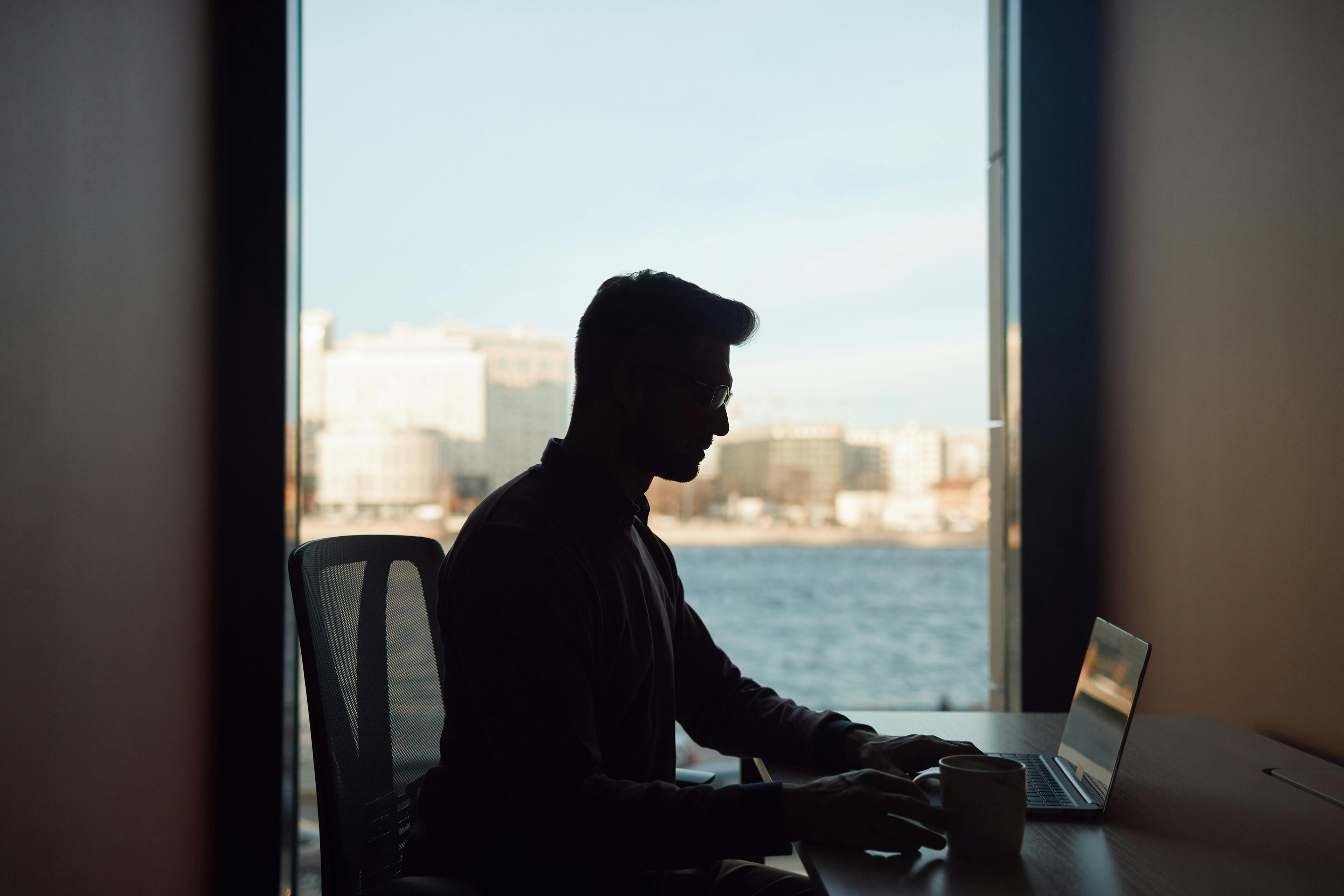 Person using a laptop at a desk by a window with water and city view