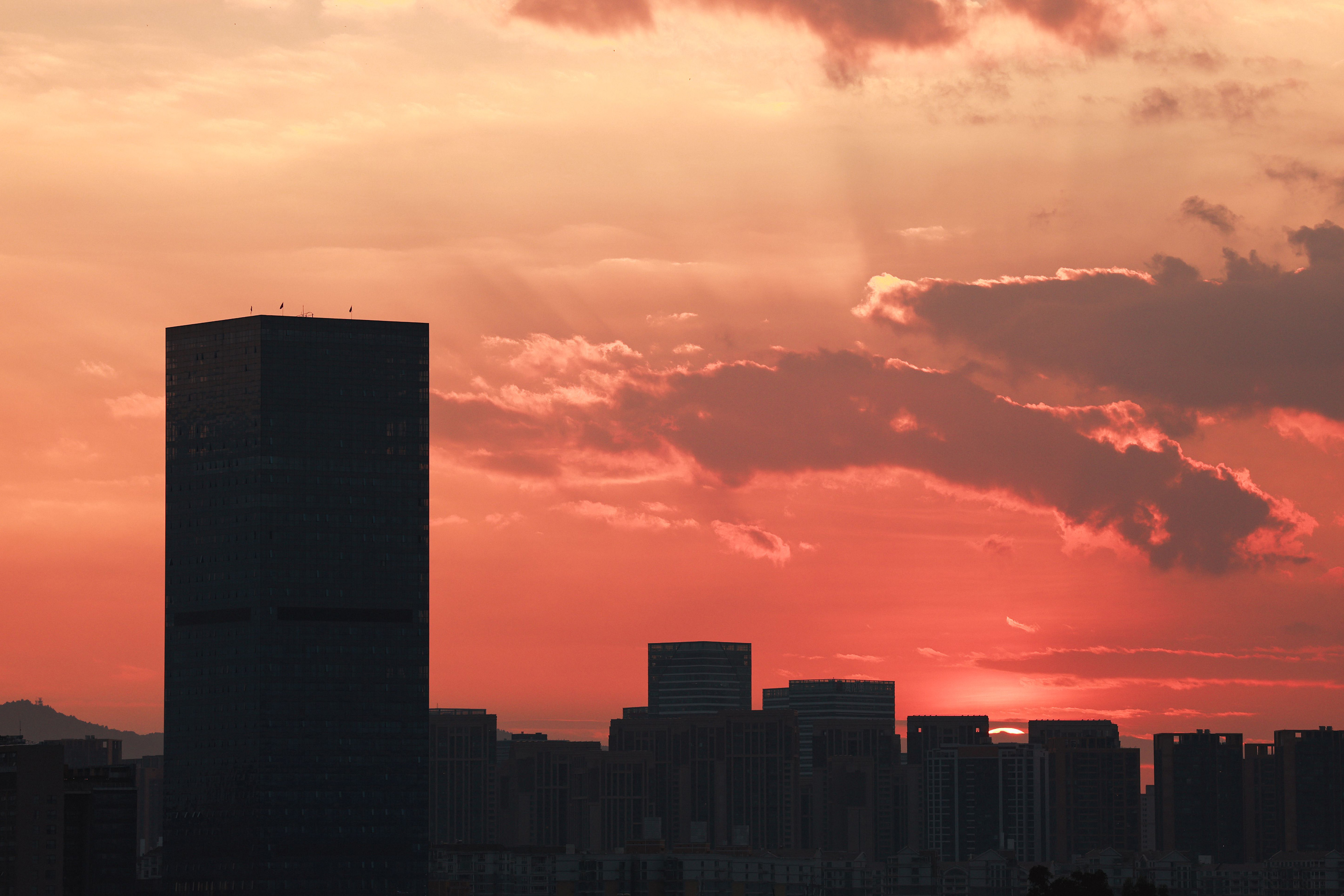 City skyline at sunset with a tall office tower silhouetted against a colorful sky